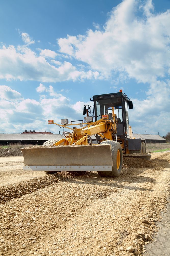 Yellow Road Grader Smoothing a Dirt Road Under a Blue Sky With Clouds — GA Plant & Automotive Repairs In Taminda, NSW
