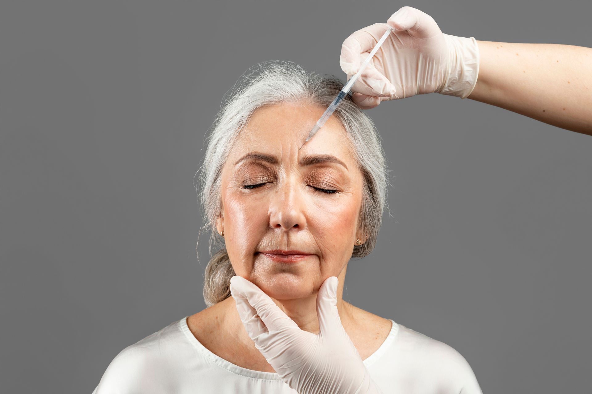 An older woman is getting a botox injection in her forehead.