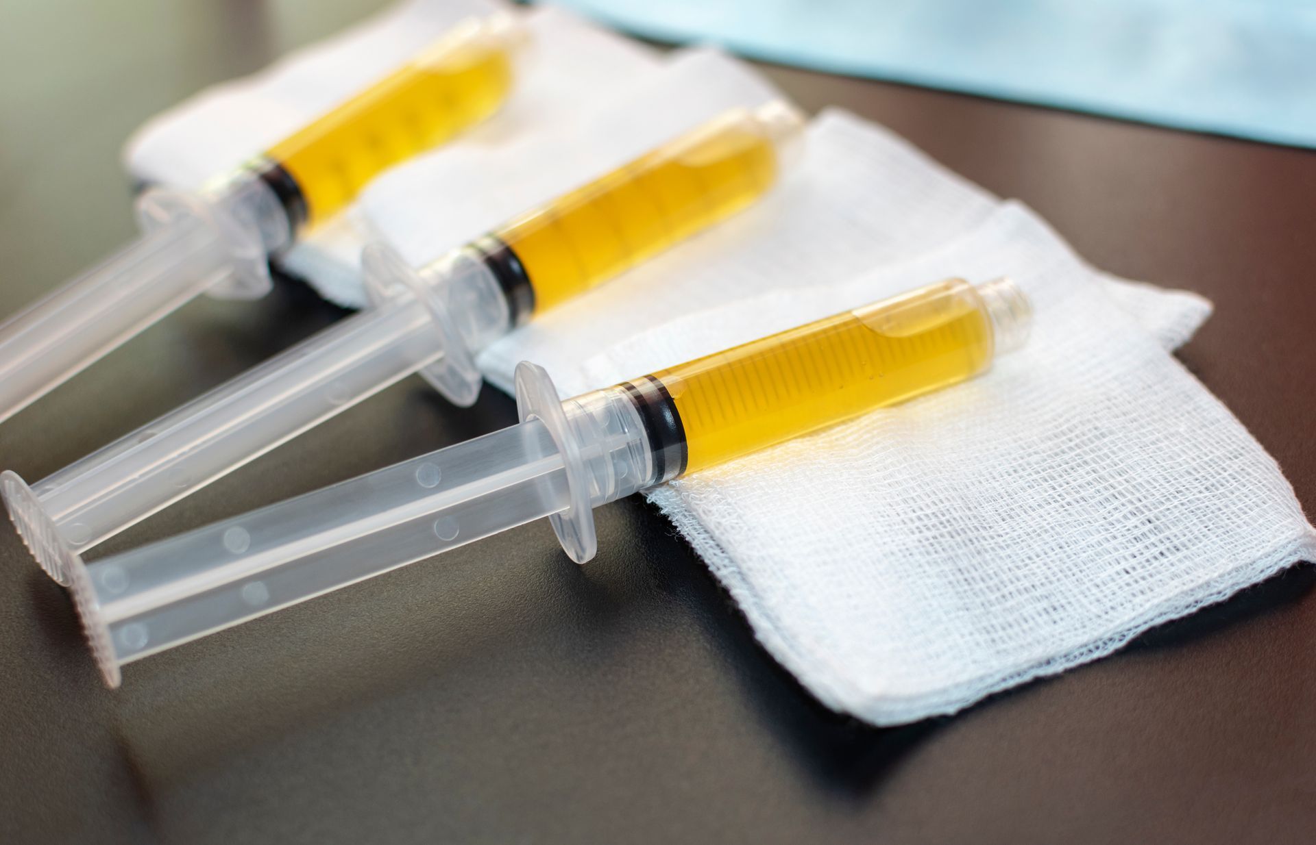 Three syringes filled with yellow liquid are sitting on a napkin on a table.