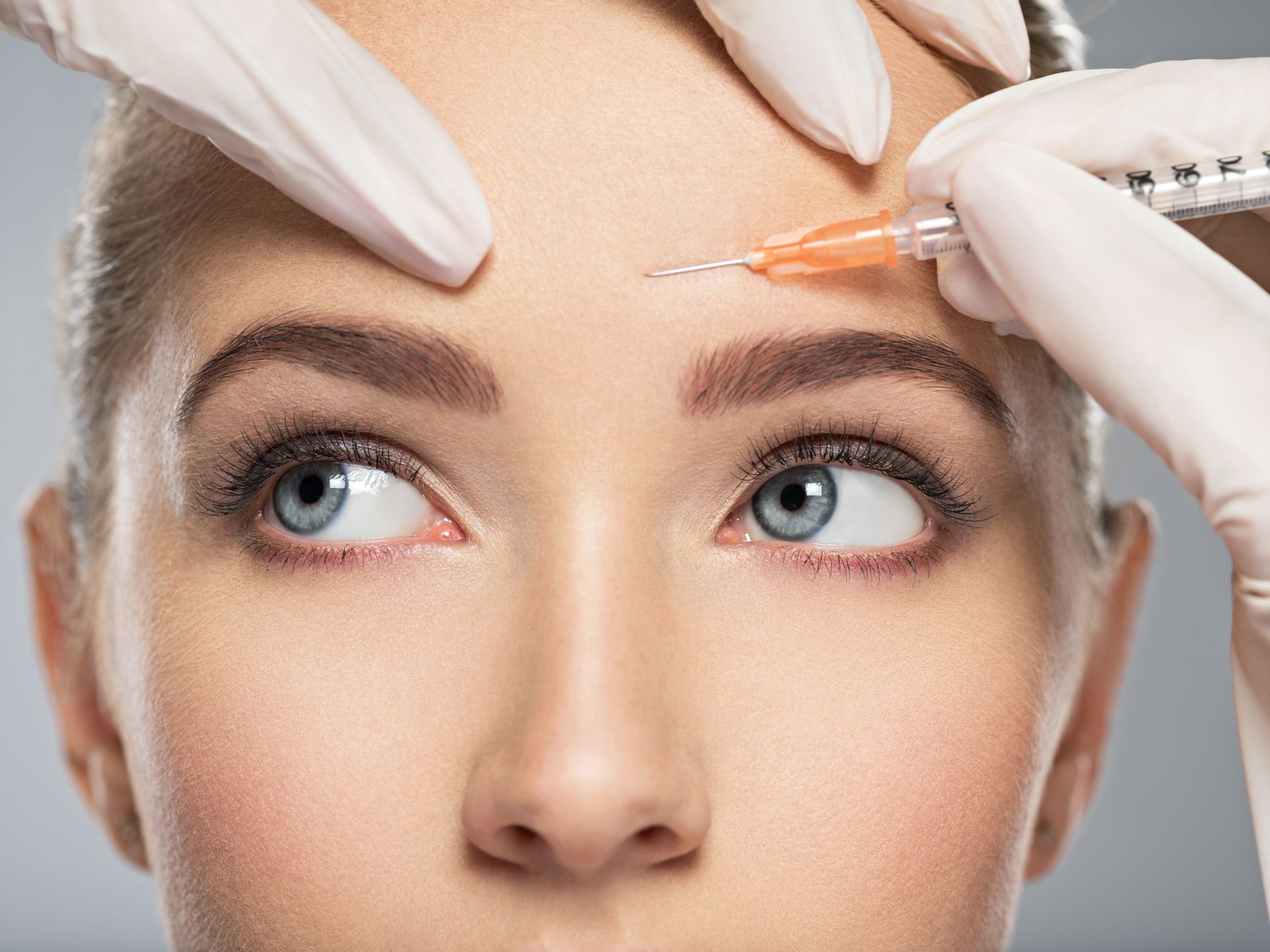 A woman is getting a botox injection on her forehead.