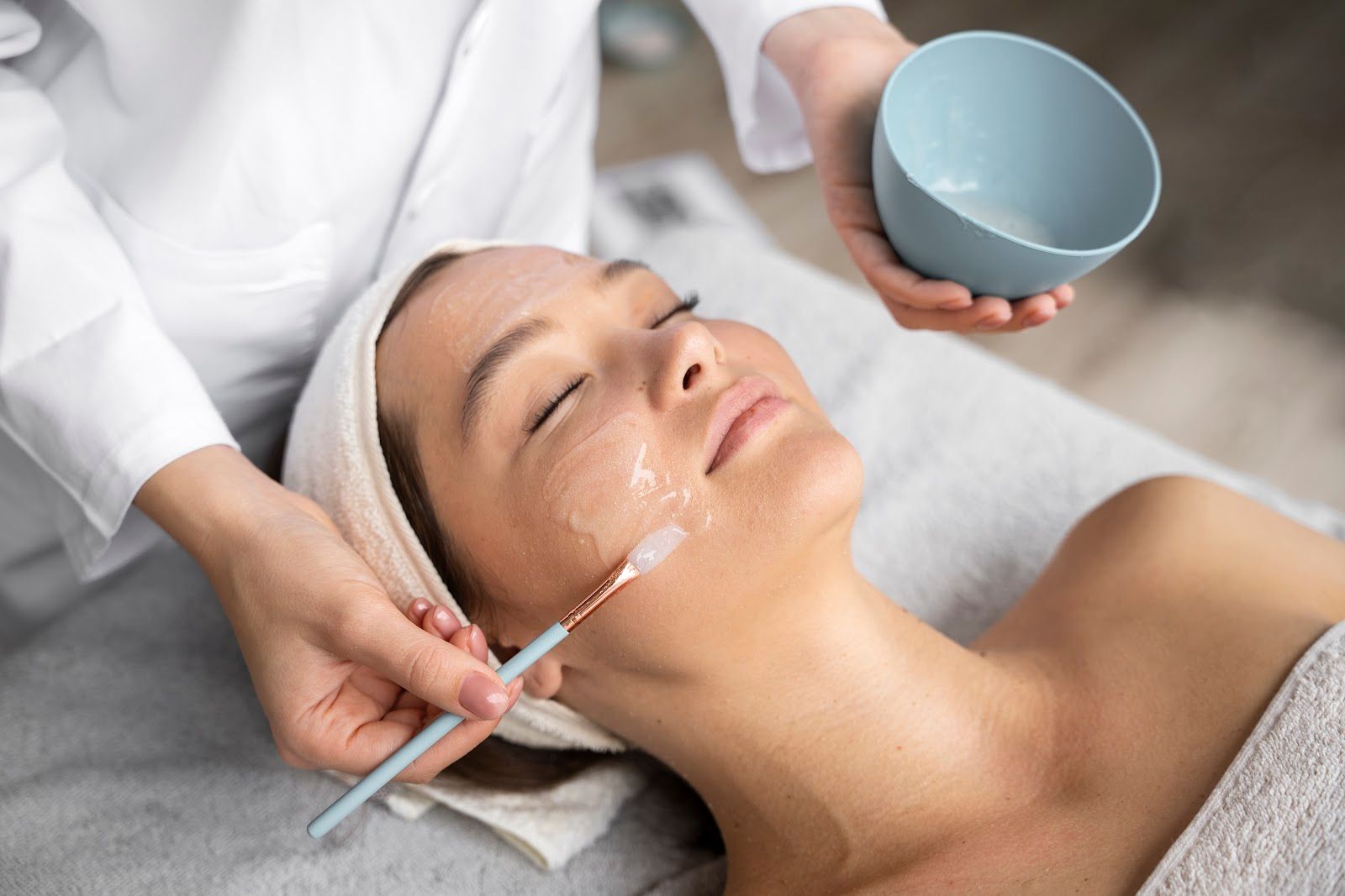 Facial treatment: Person receiving skincare with brush and bowl held by professional in spa setting.