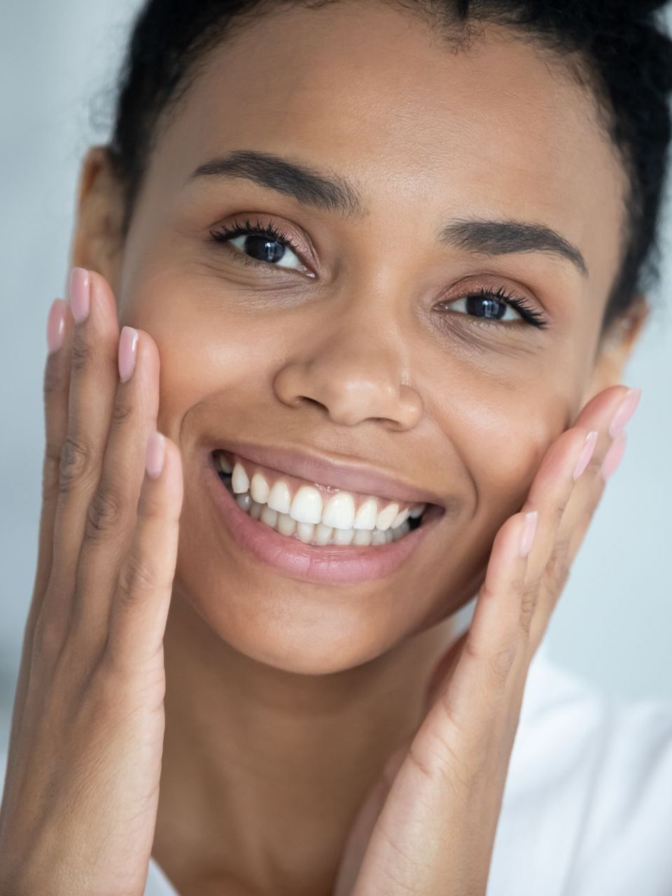 A woman is smiling and touching her face with her hands.