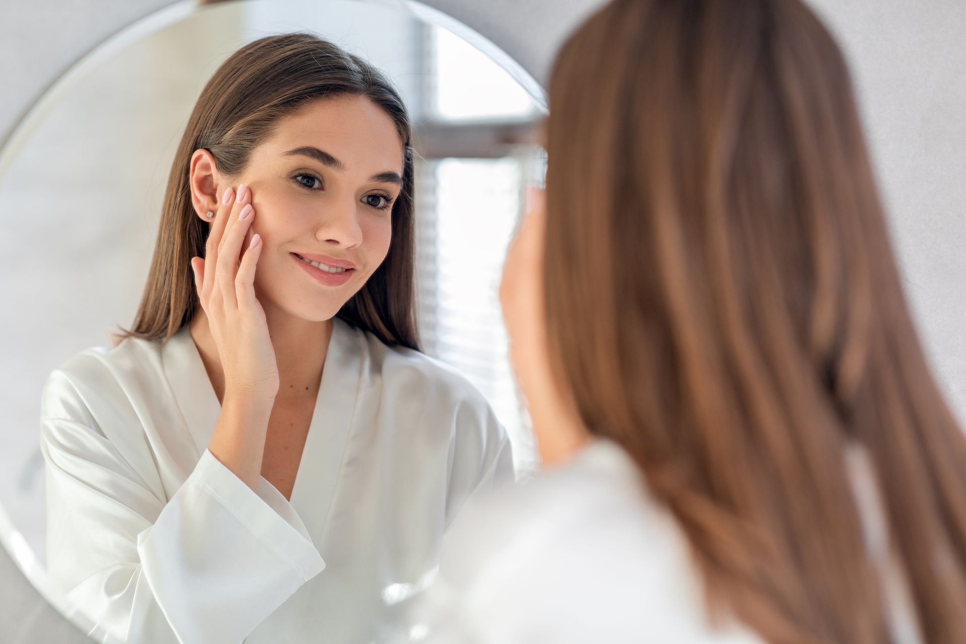 A woman is looking at her face in a mirror.