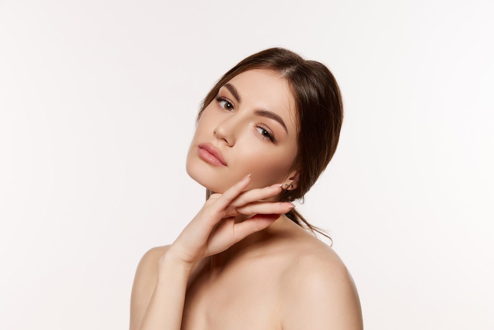 Woman with brown hair, hand near face, bare shoulders, soft lighting.
