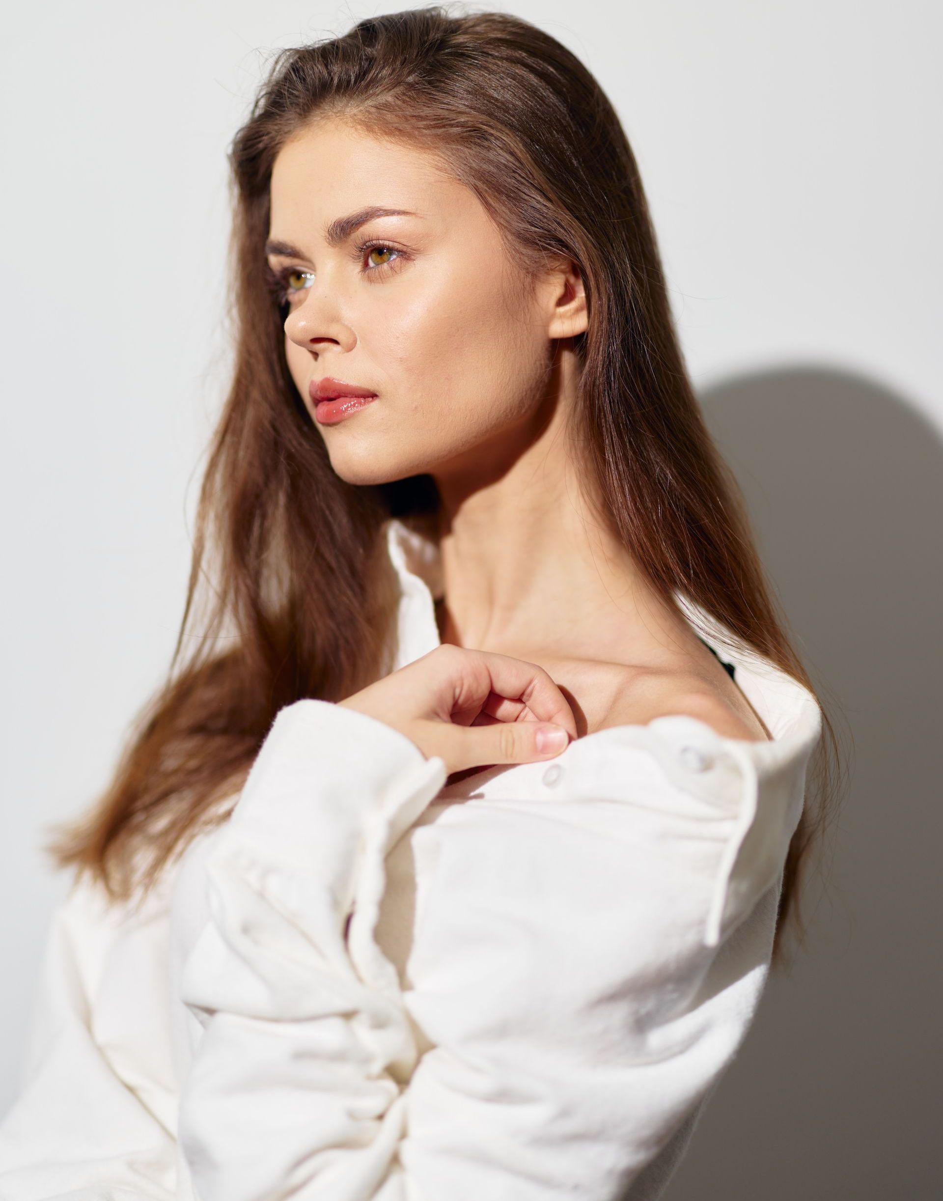 A woman in a white sweater is standing in front of a white wall.