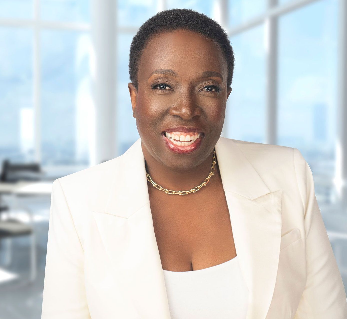 Photo of Dr. Judith Josiah-Martin, a woman of color with dark skin wearing a white pant suit smiling in a modern office room