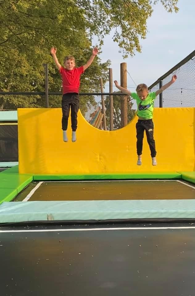 Two young boys are jumping on a trampoline.