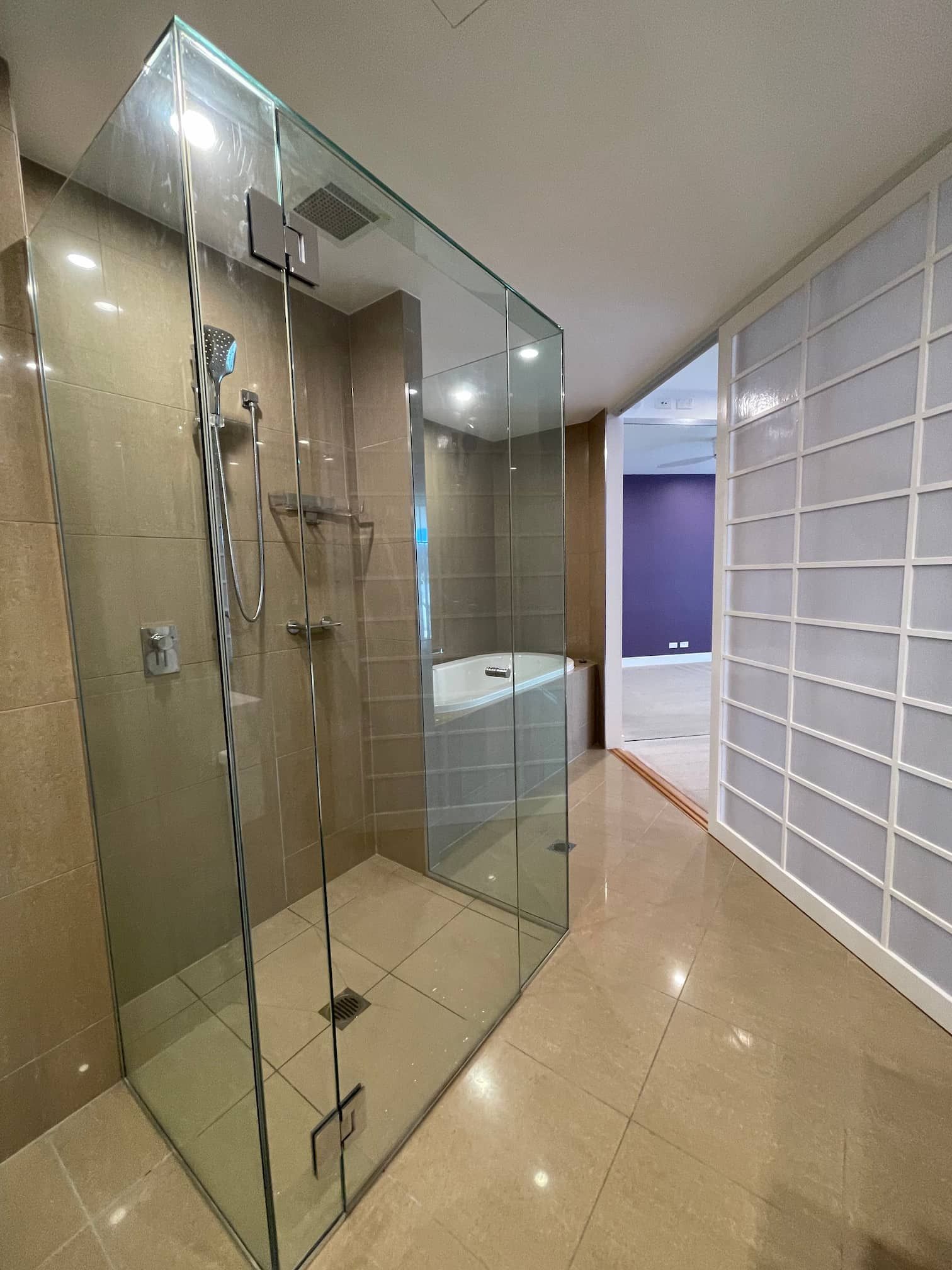 Modern bathroom with a glass shower enclosure, tiled walls and floor, and a white tub.