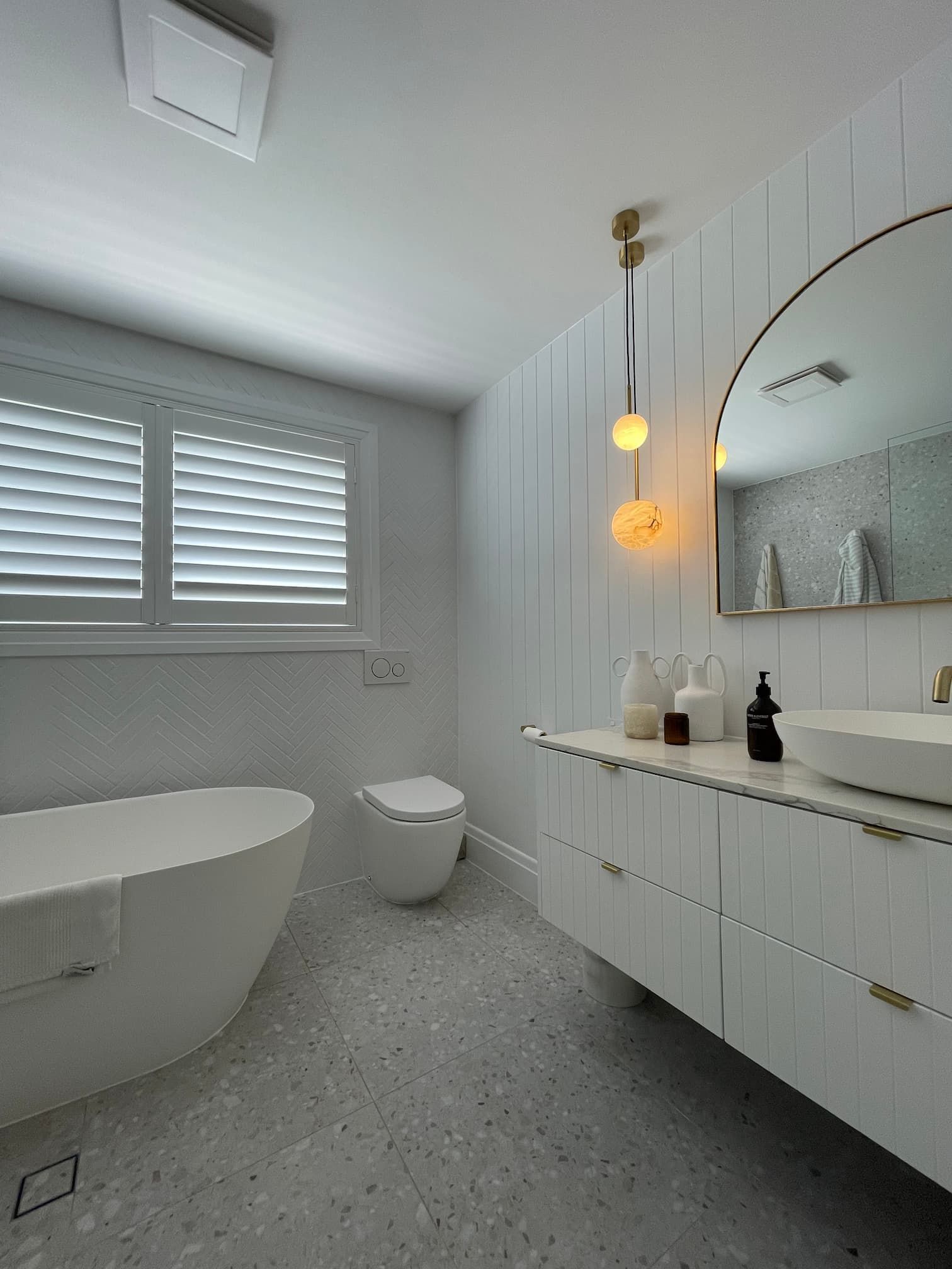Modern white bathroom with freestanding tub, floating vanity, and terrazzo floor.