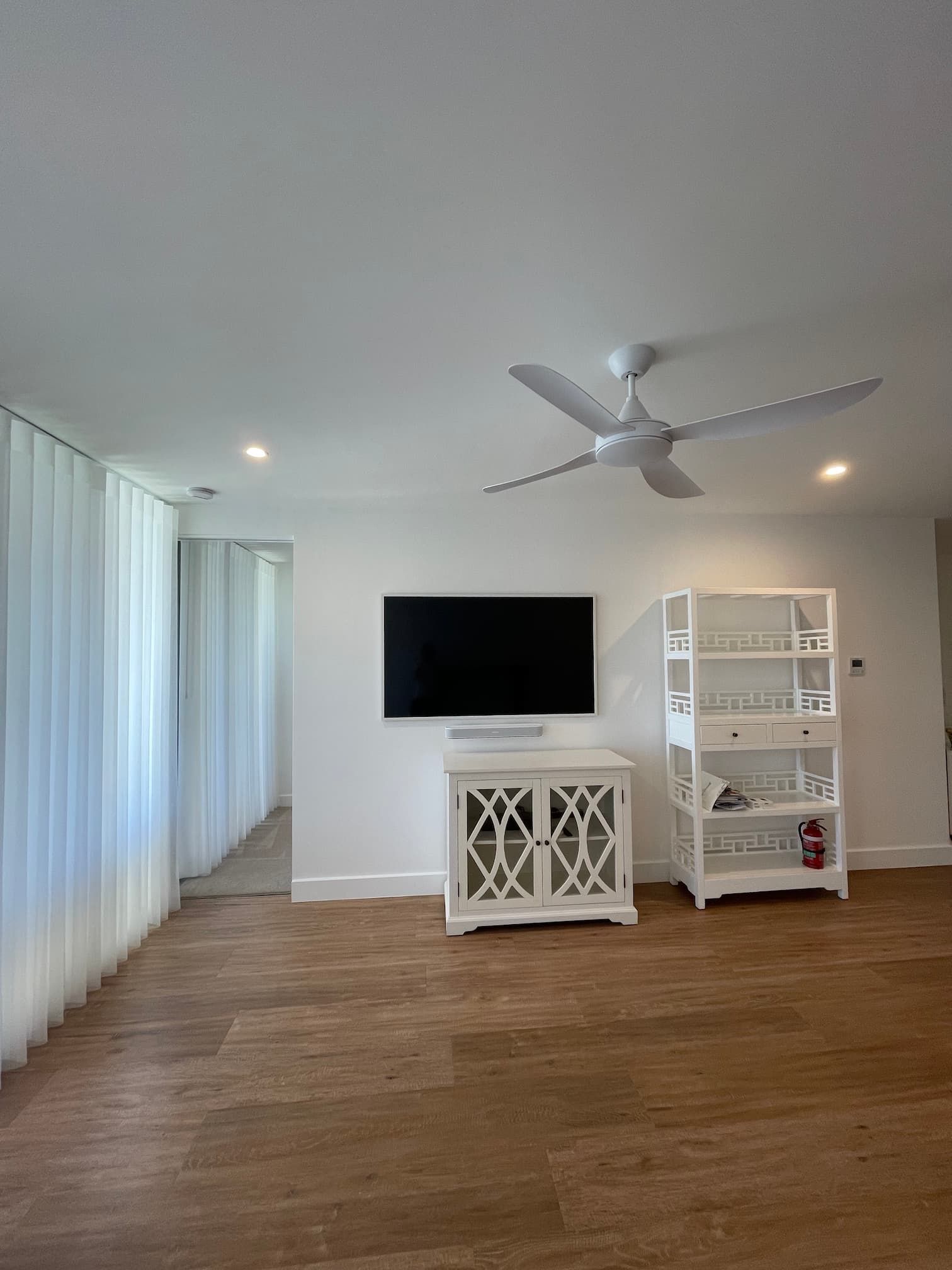 Living room with white walls, wooden floor, TV above a white cabinet, and a white shelving unit.