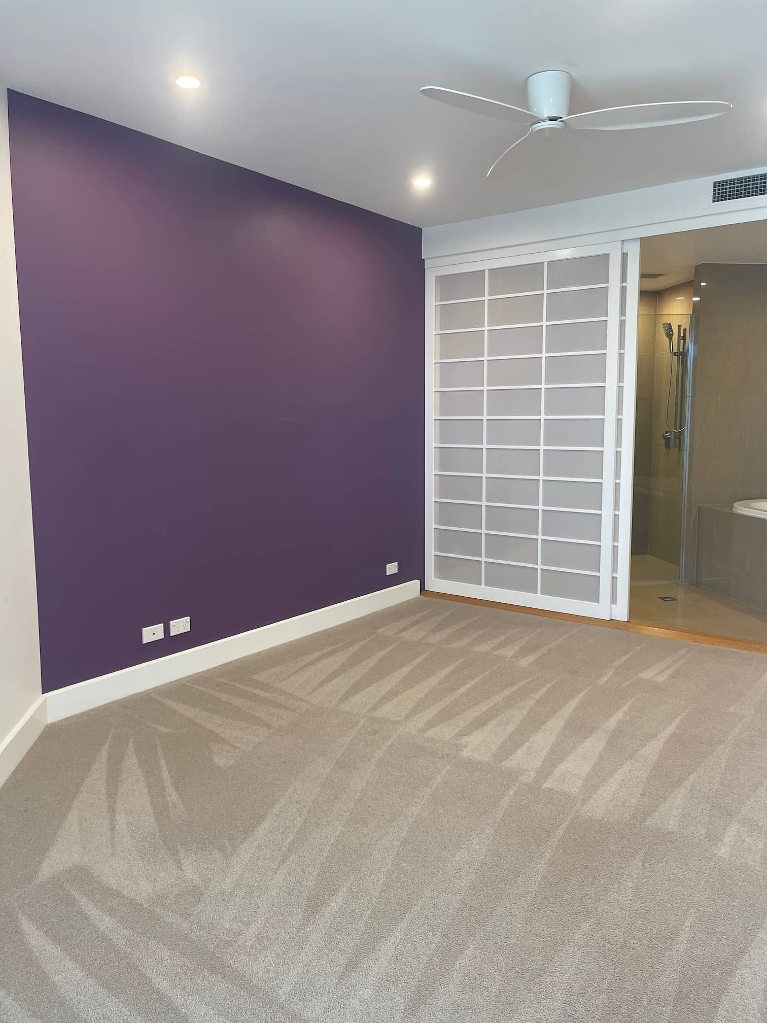 A bedroom with purple accent wall, beige carpet, and a sliding white screen.