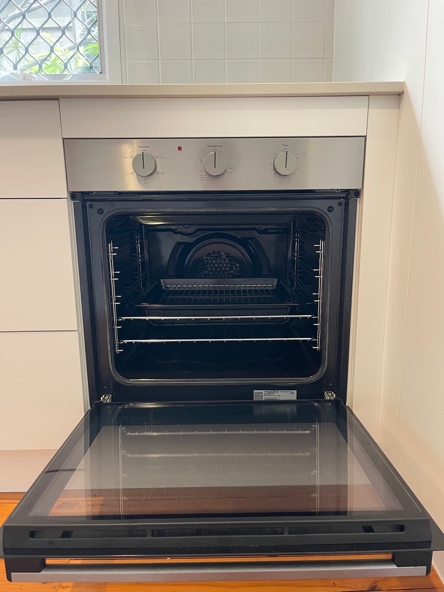 Open oven in a kitchen. Stainless steel face with three knobs.