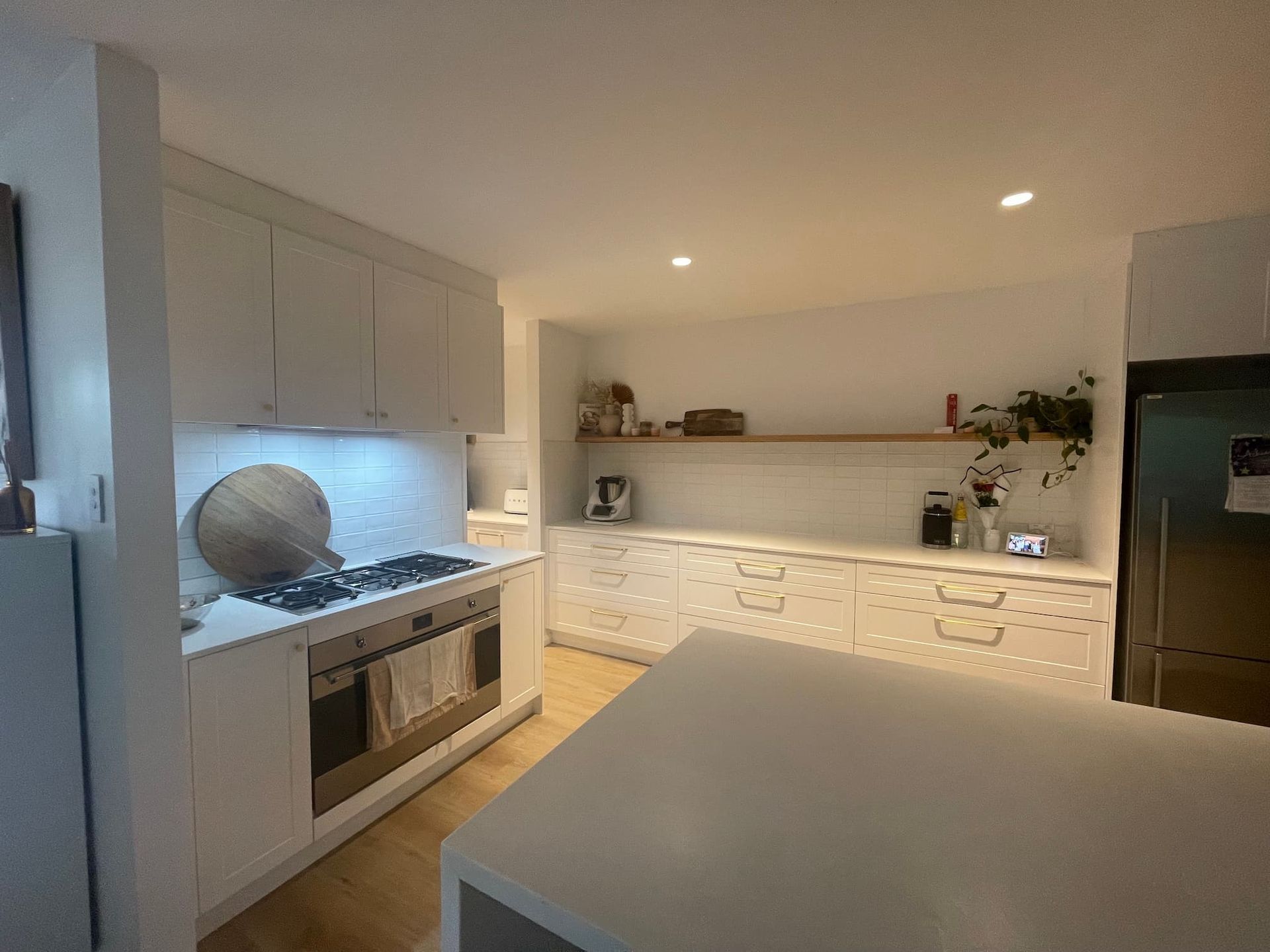 White kitchen with island, cabinets, stove, and refrigerator. Wooden countertop and shelves.