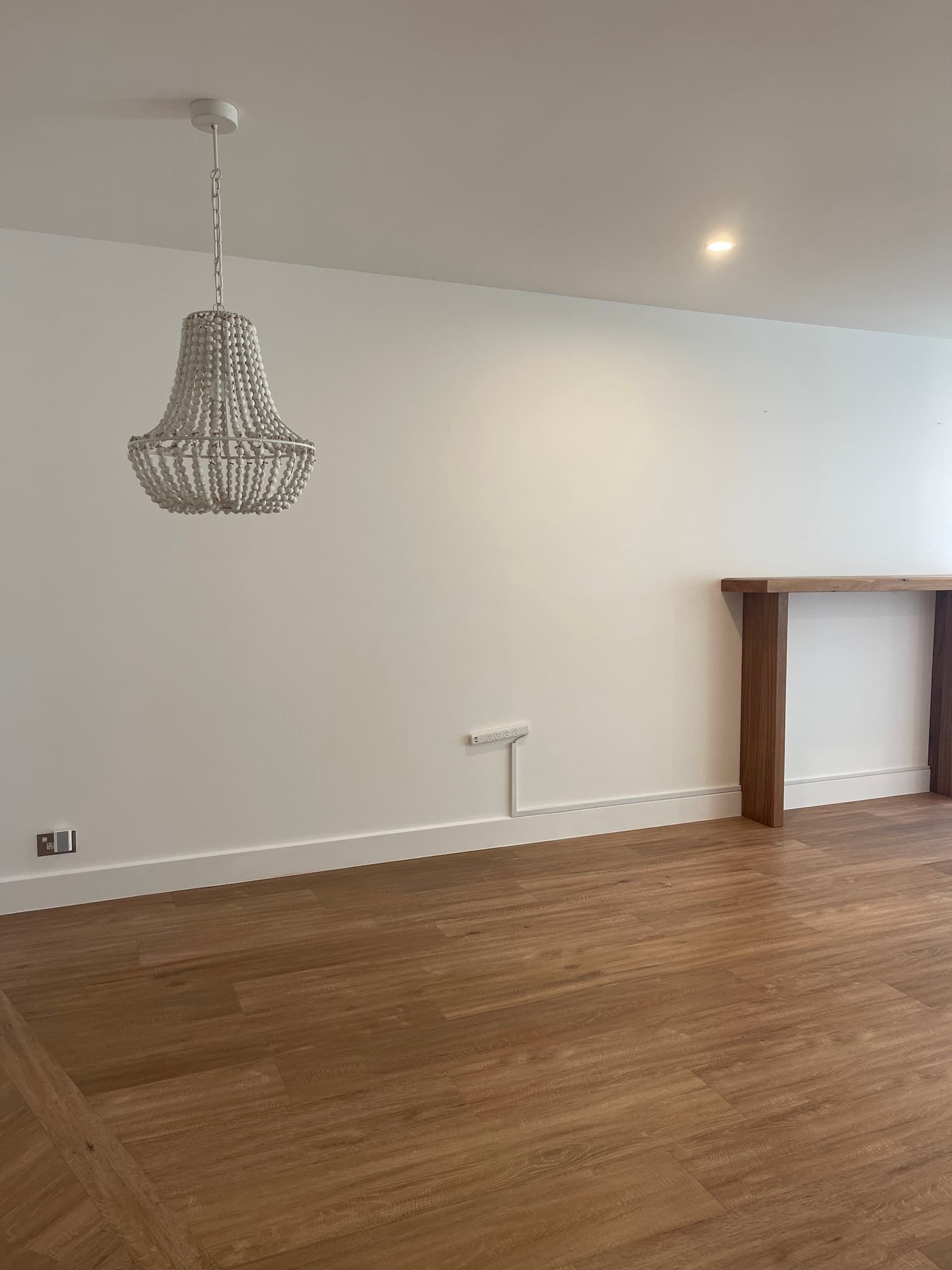 A room with a wooden floor, white walls, and a decorative chandelier. A wooden mantle is on the right.