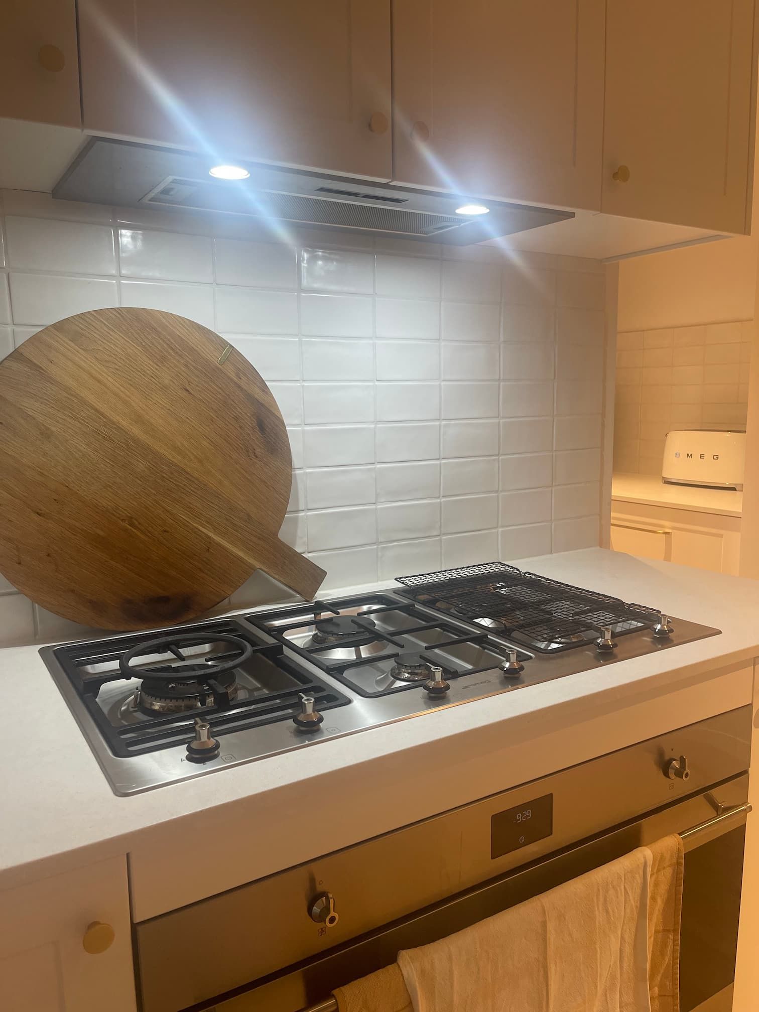 Kitchen with a stainless steel stovetop and oven. A wooden cutting board rests against white subway tile.