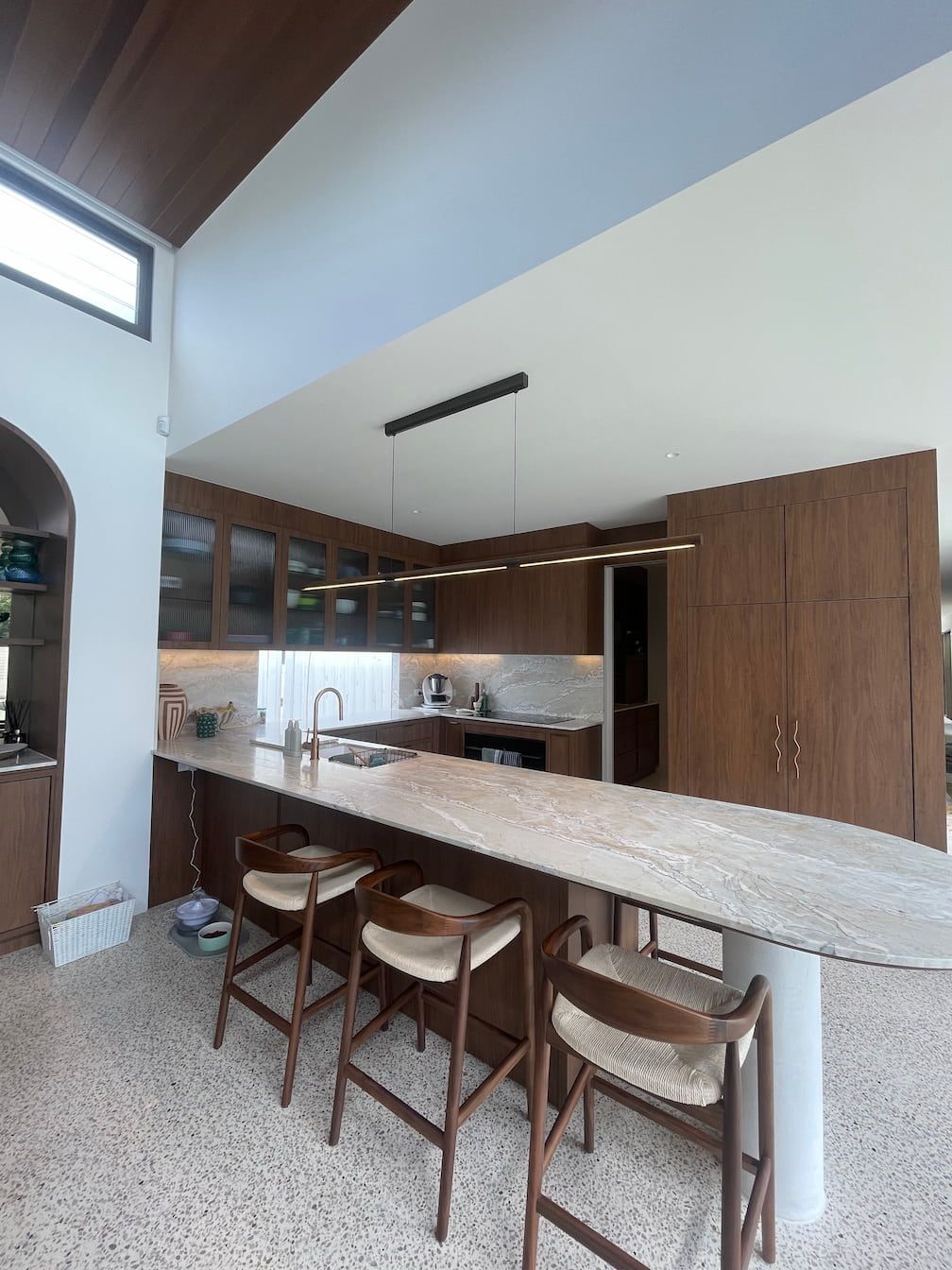 Modern kitchen with wooden cabinetry, marble countertops, and a large island with bar stools.
