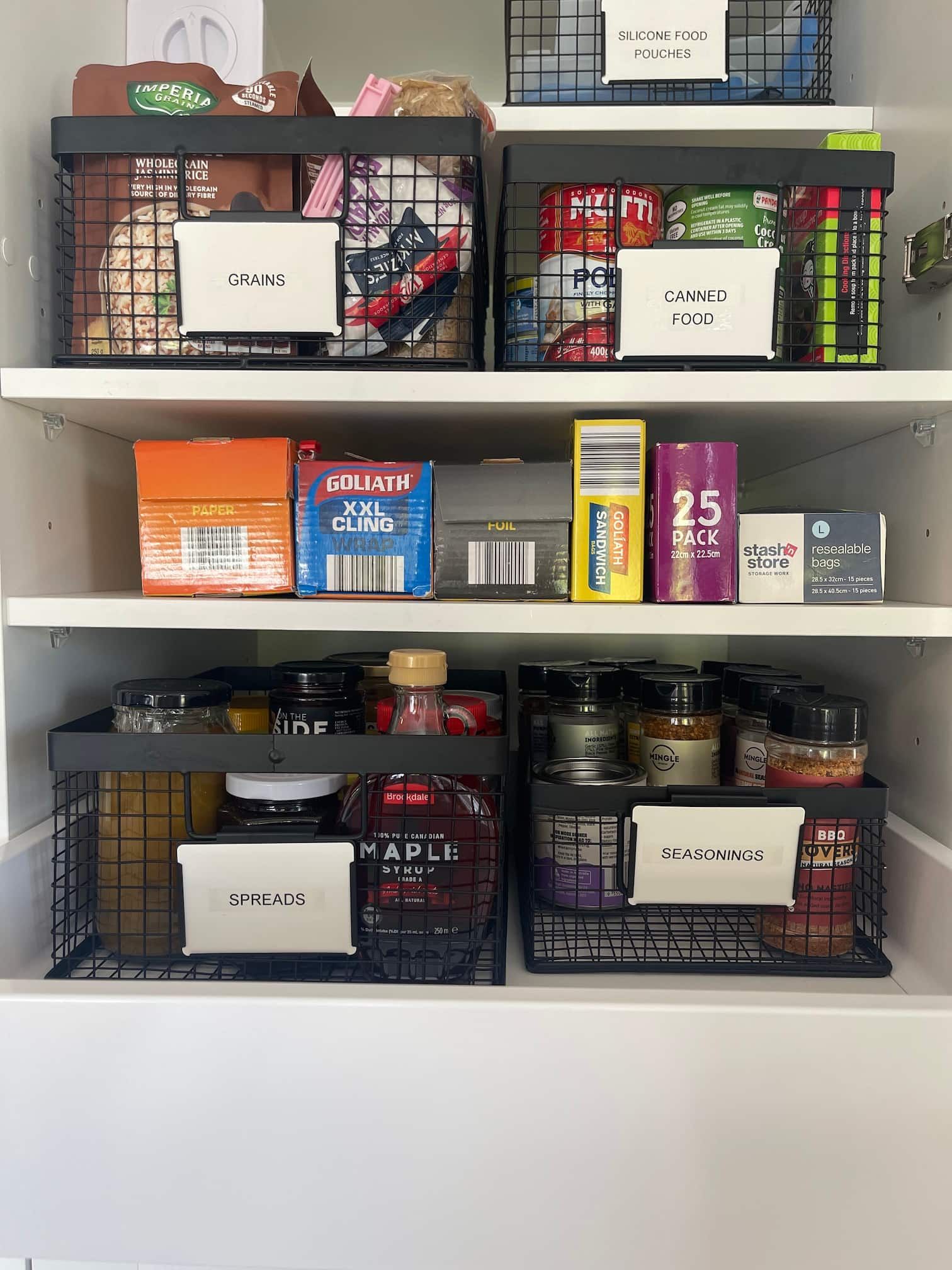 A neatly organised pantry with wire baskets labeled for snacks, sides, and spices.