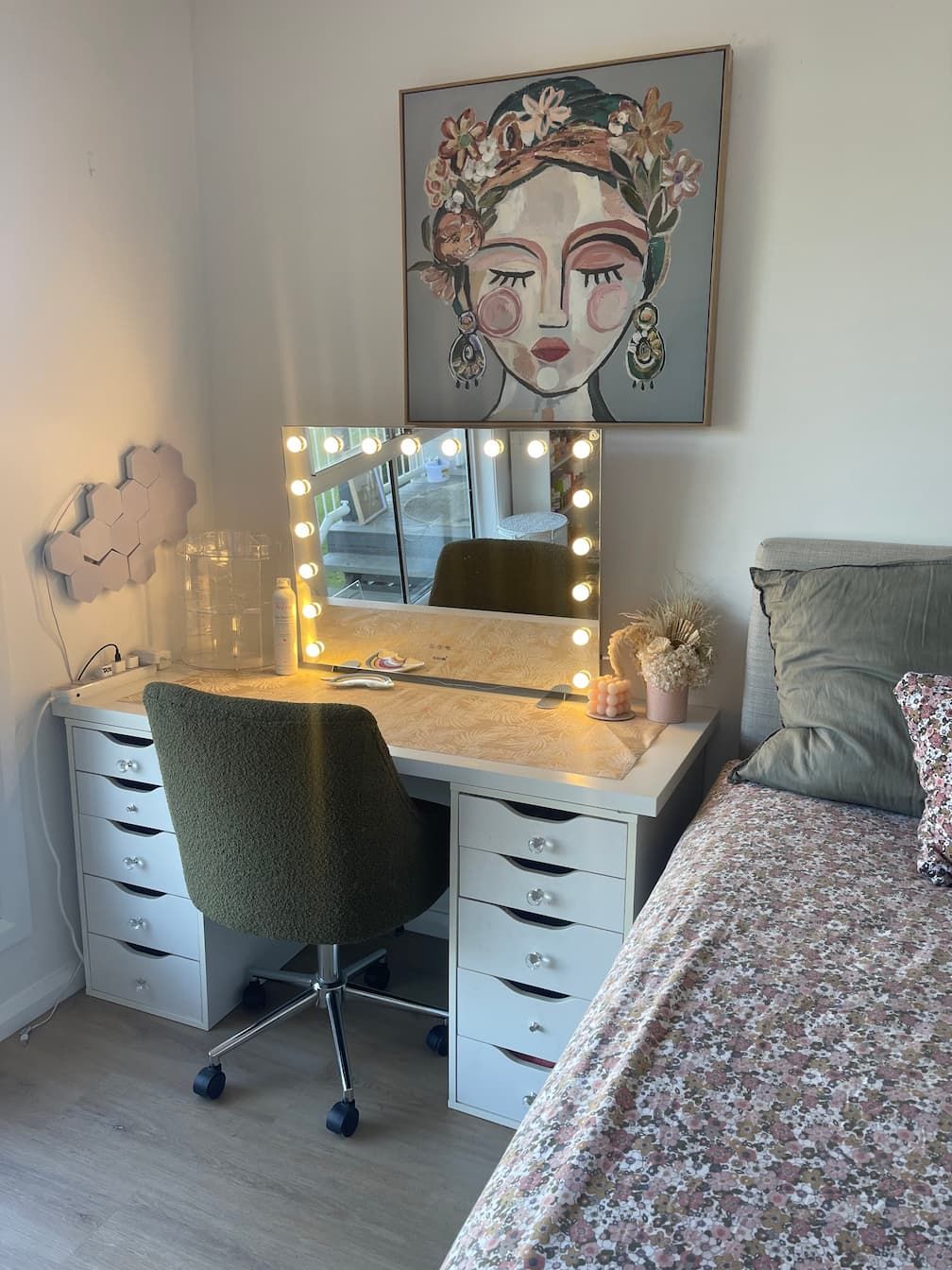Makeup vanity with a lighted mirror, chair, and artwork in a bedroom.