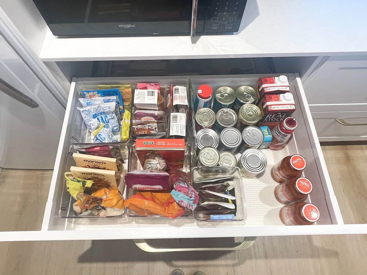 Organised kitchen drawer filled with clear bins holding snacks and canned goods.
