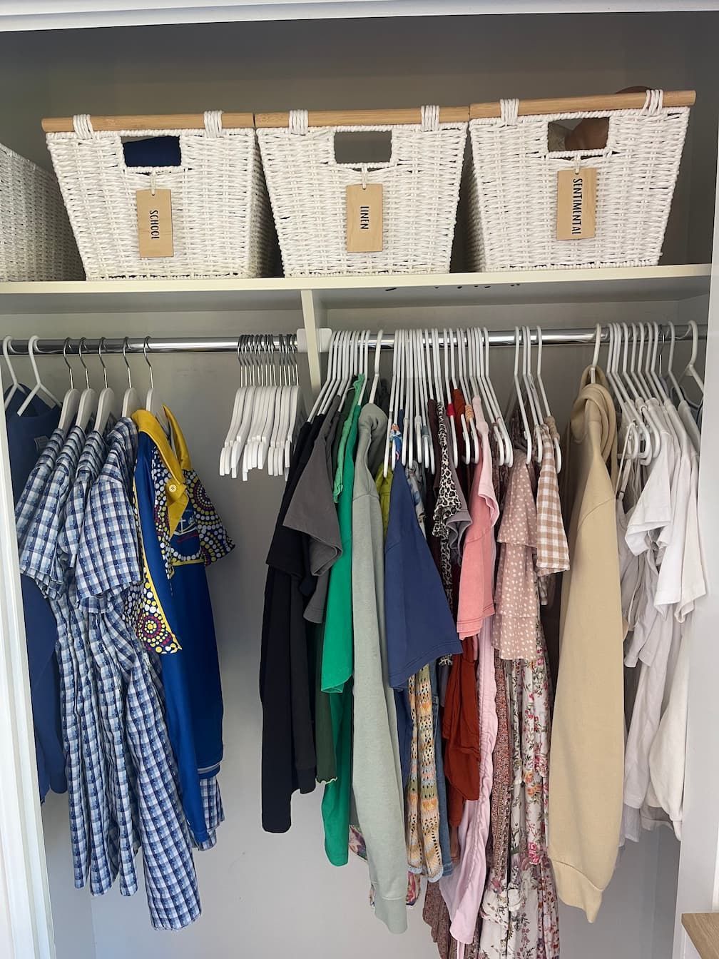 A closet with clothes hanging on rods and baskets on a shelf.