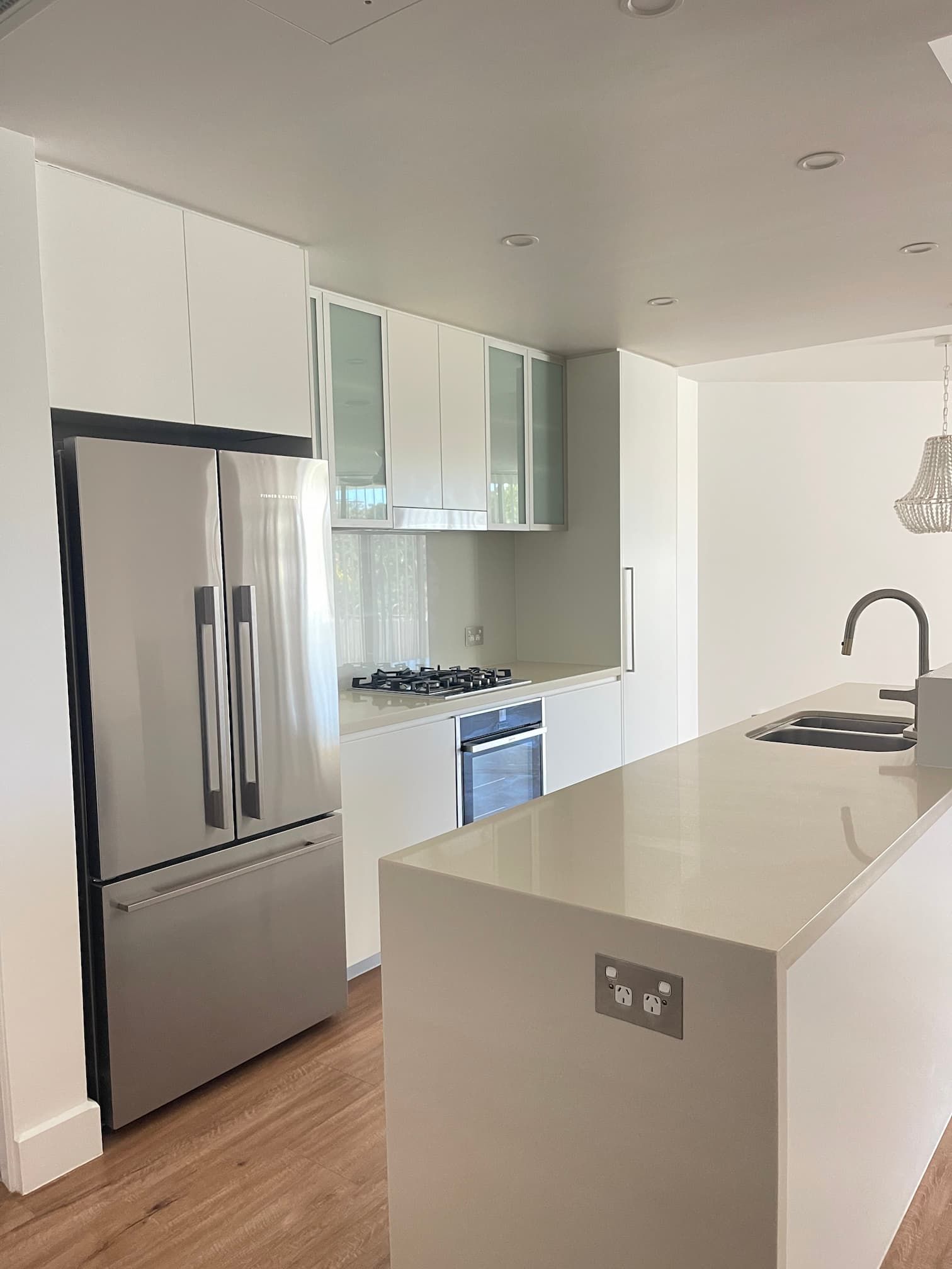 Modern white kitchen with stainless steel refrigerator, stovetop, and island. Light wood flooring.