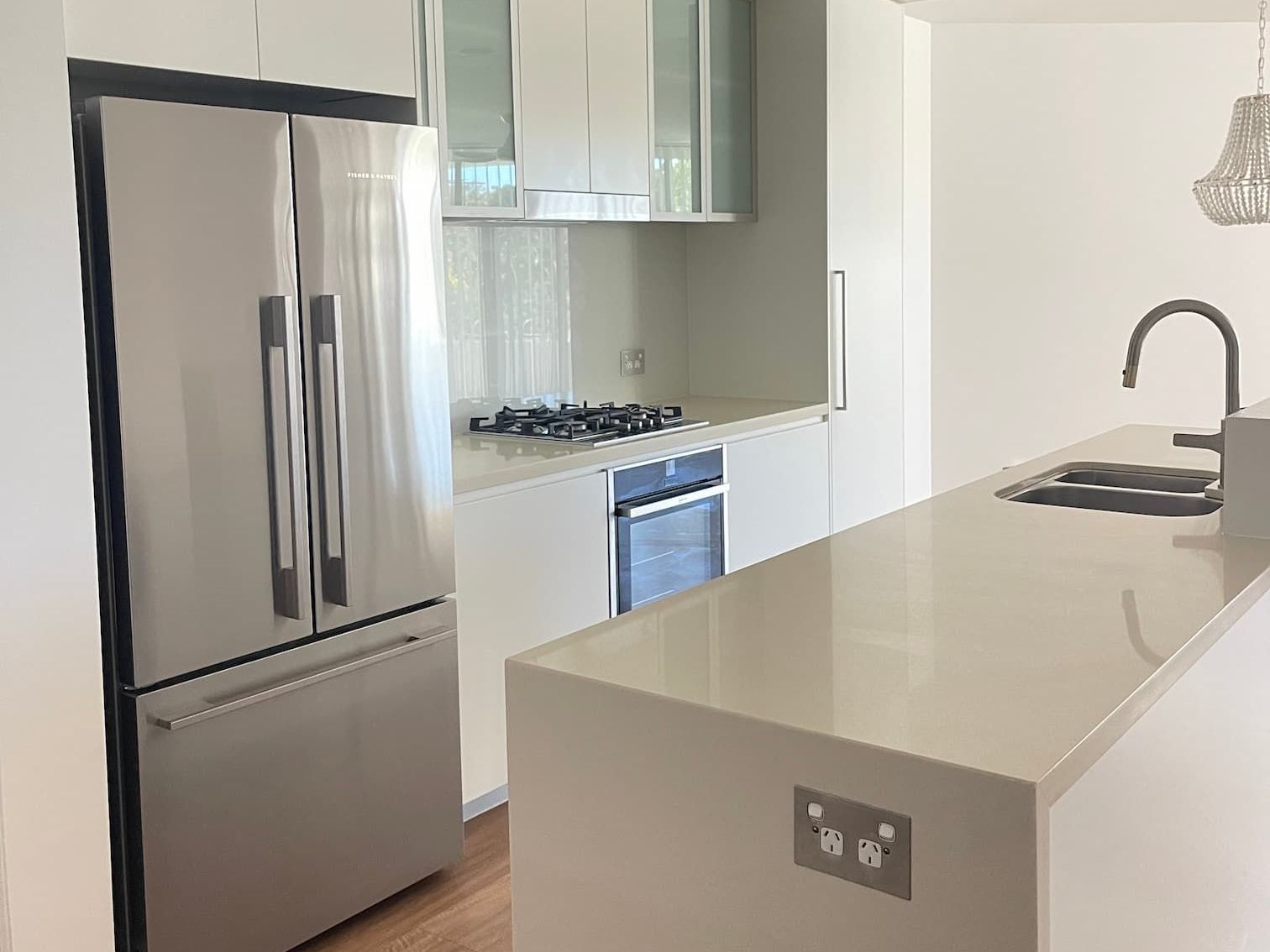 Modern kitchen with stainless steel refrigerator, white cabinets, and a light-colored countertop island with a sink.
