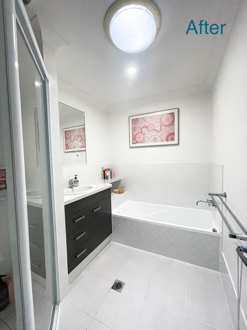Bright white bathroom with a dark vanity, tub, and shower, and art on the wall; the word