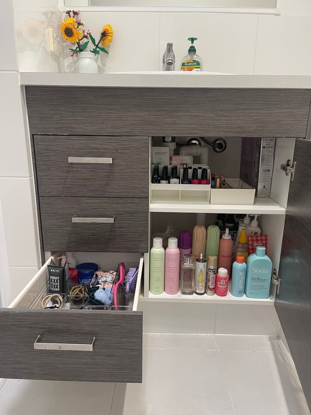 Bathroom vanity with open drawers and cabinet, revealing toiletries and beauty products in various containers.