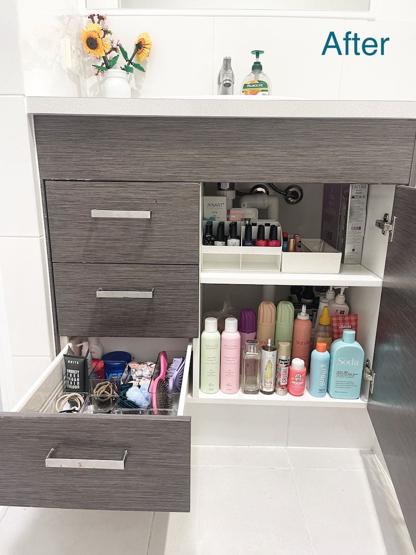 Bathroom cabinet with open drawer showing toiletries. Gray cabinet with organized products like shampoo and makeup.