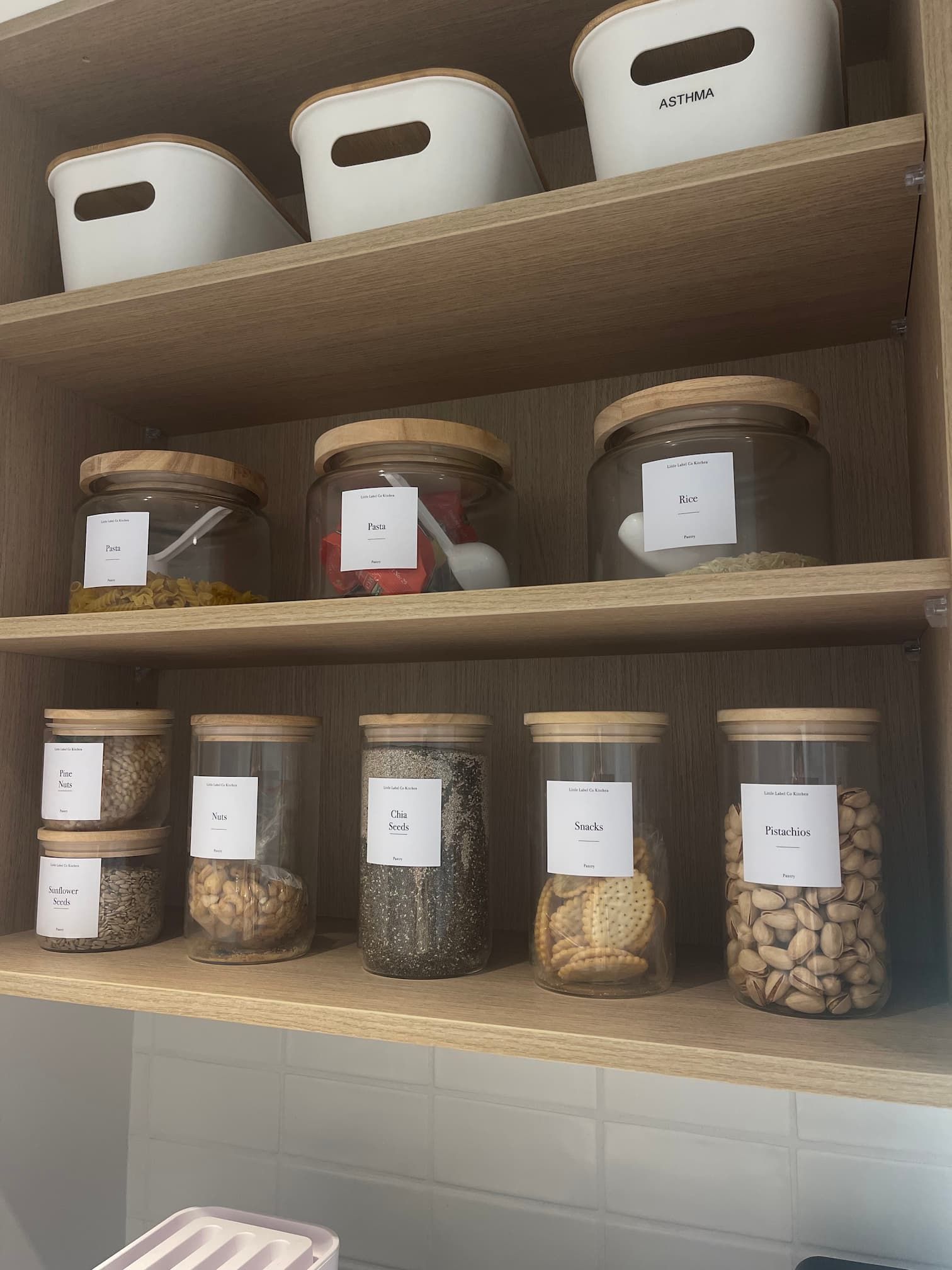 Wooden shelves filled with clear glass jars and white containers, neatly organized with labels.