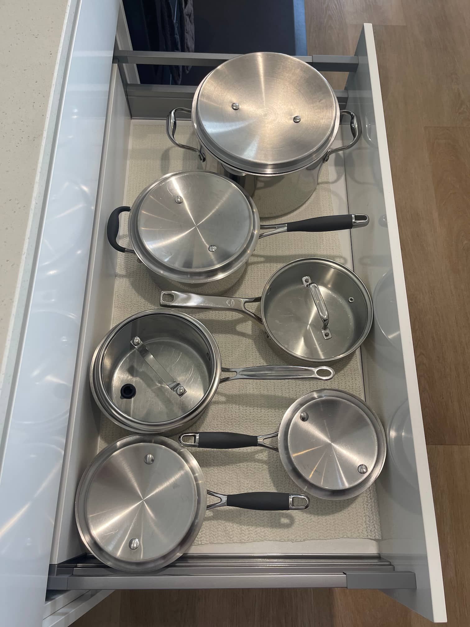 A drawer filled with stainless steel pots and pans, lids included, neatly organized inside a kitchen cabinet.