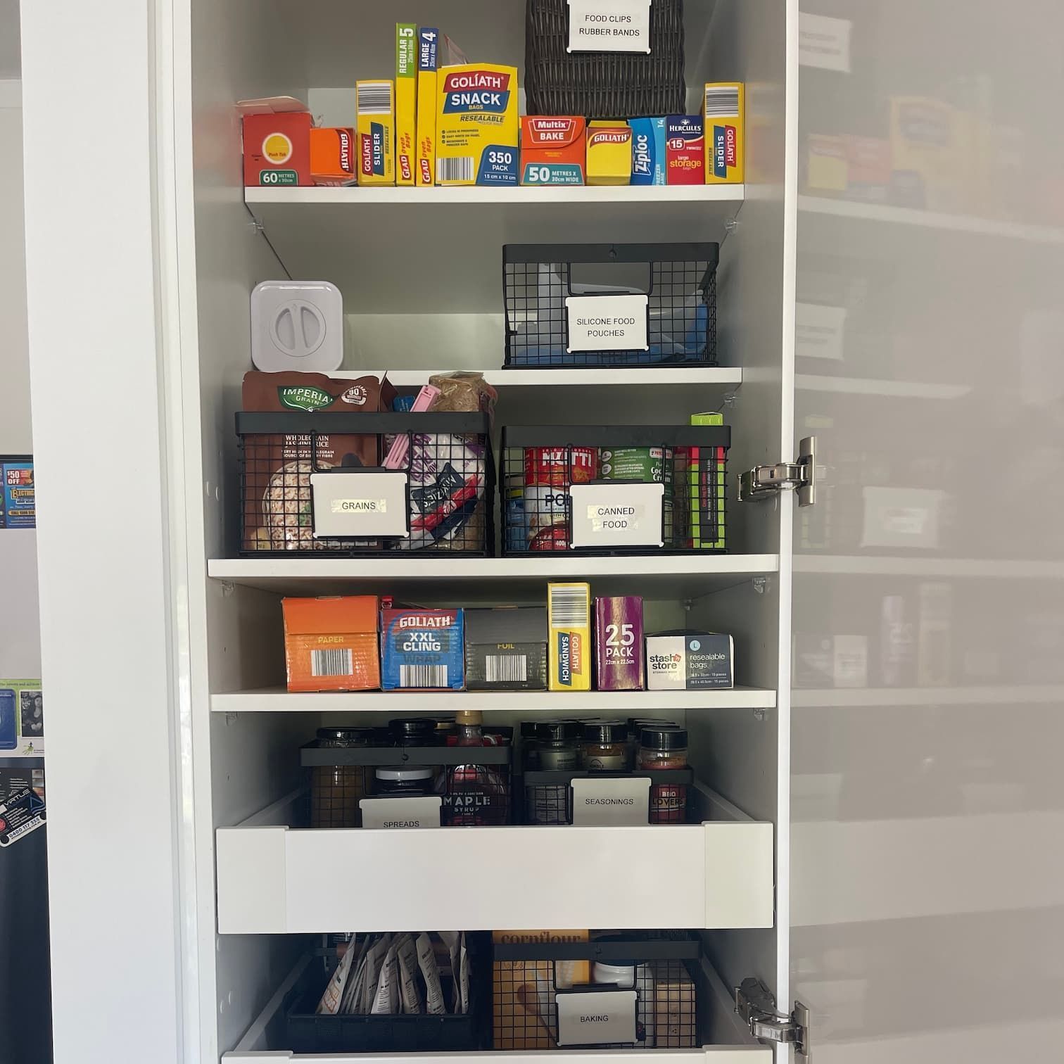 White pantry cabinet with organized shelves. Various food items are stored in labeled containers and baskets.
