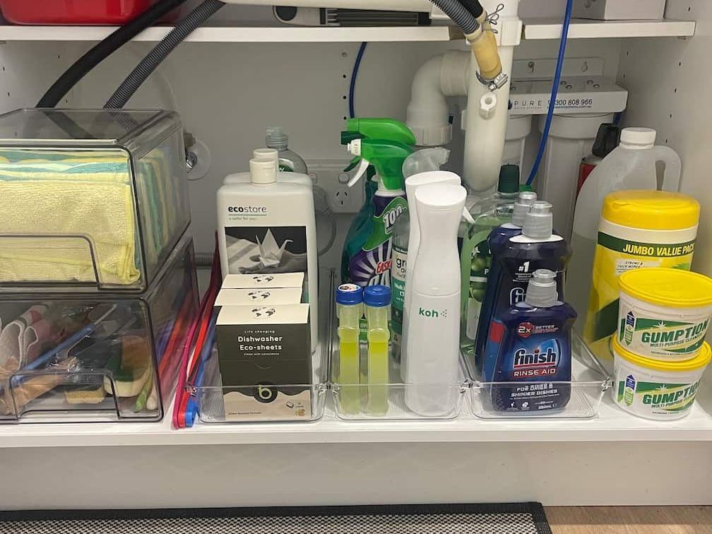 Cleaning supplies organized under a sink: bottles, sprayers, sponges, and containers in clear bins.