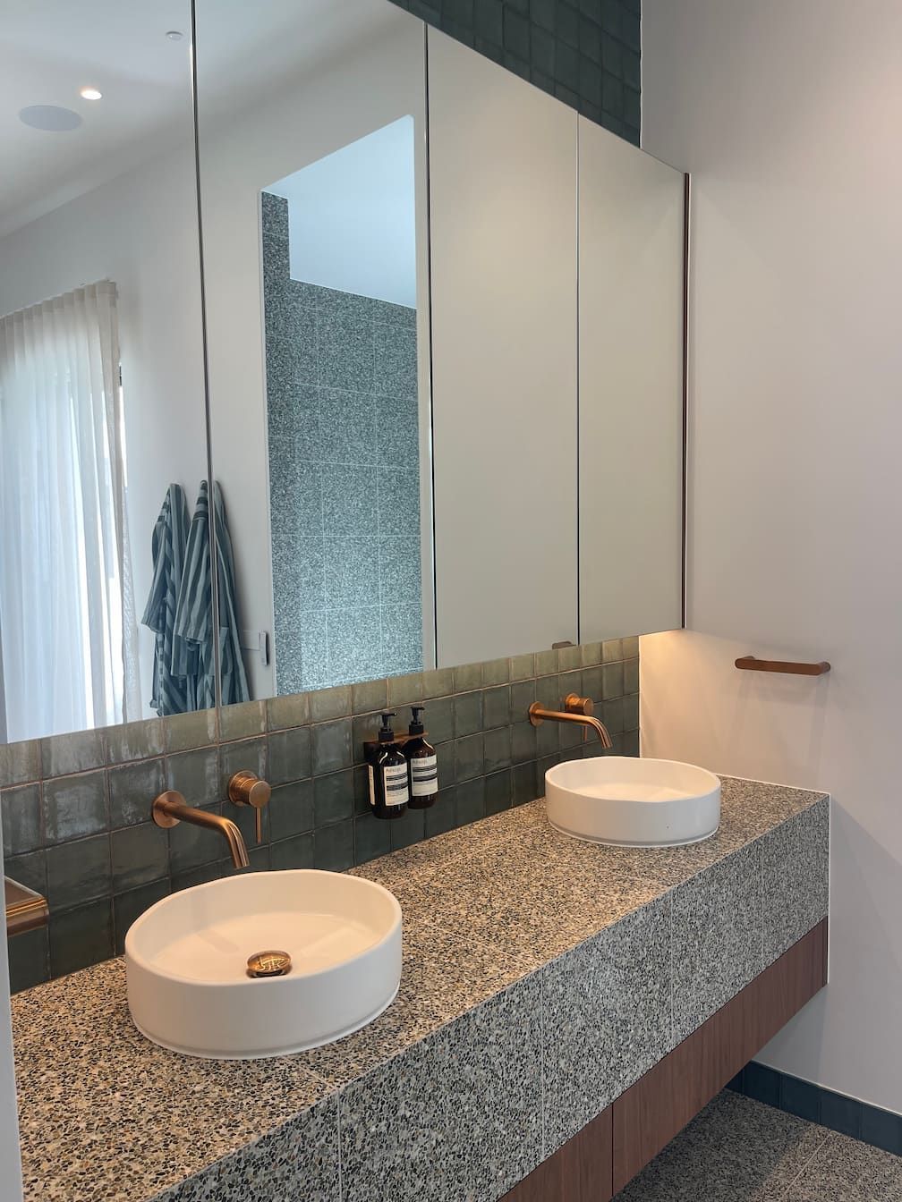 Bathroom with dual white sinks, copper faucets, gray countertop, and large mirror.