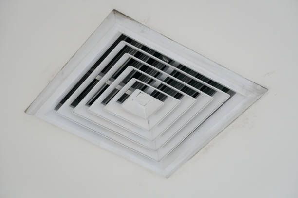 A white, square air vent with black slats in a white ceiling.