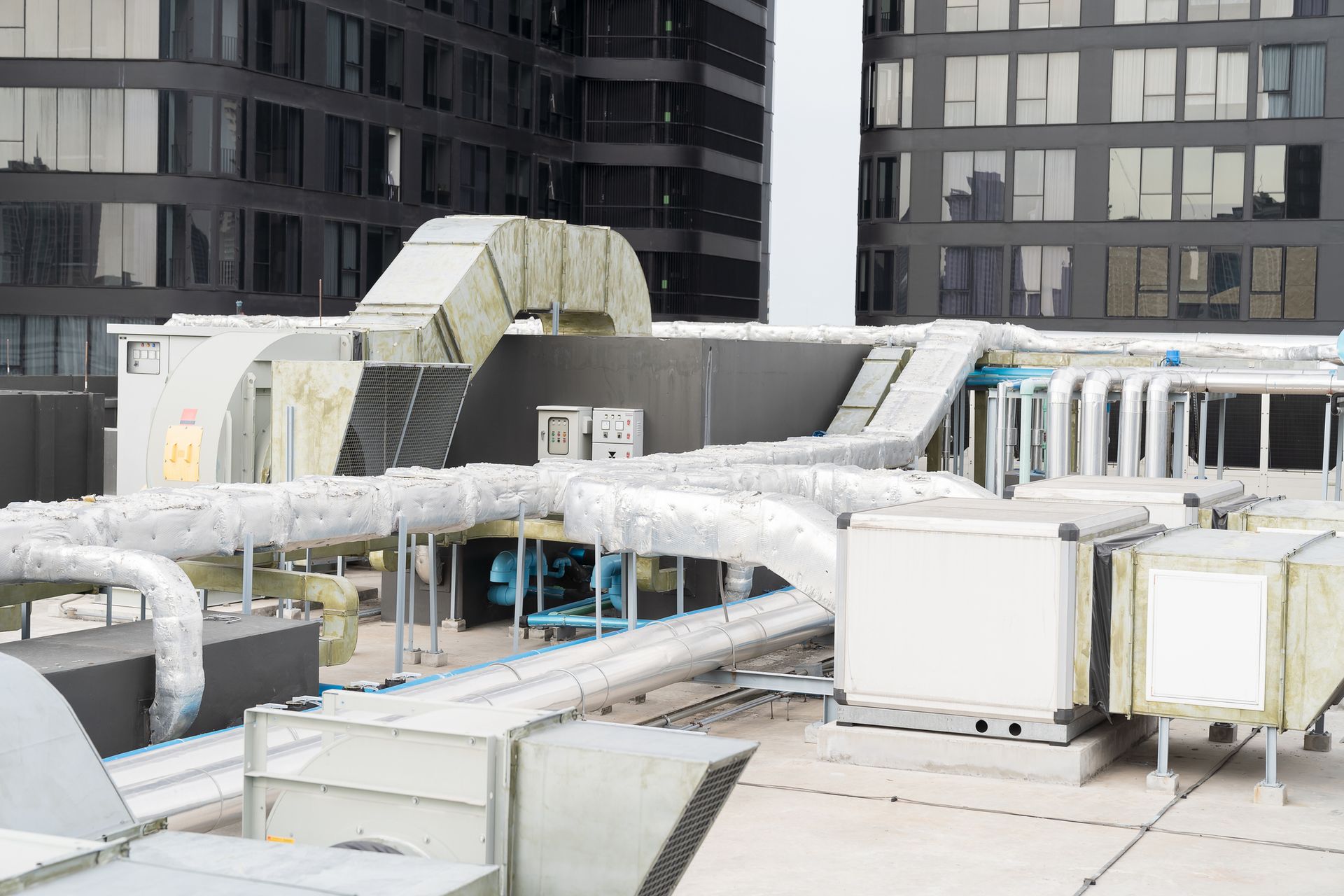 Rooftop HVAC system with ductwork, vents, and equipment against a backdrop of a modern building. Gray and silver tones dominate.