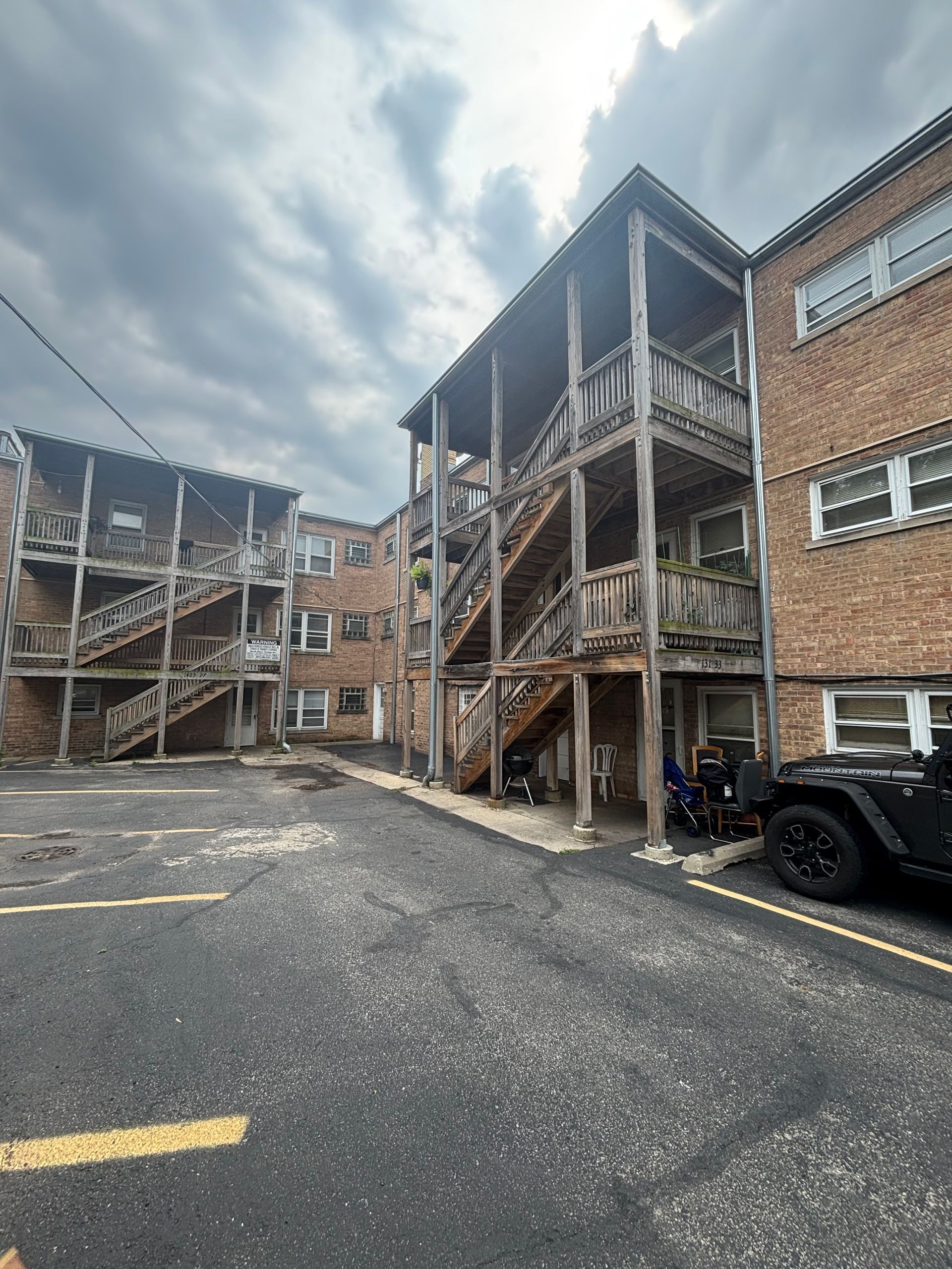 Apartment building exterior with wooden staircases and a parking lot on a cloudy day.
