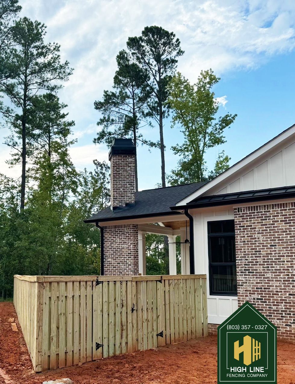 A wooden fence surrounds a driveway with trees in the background