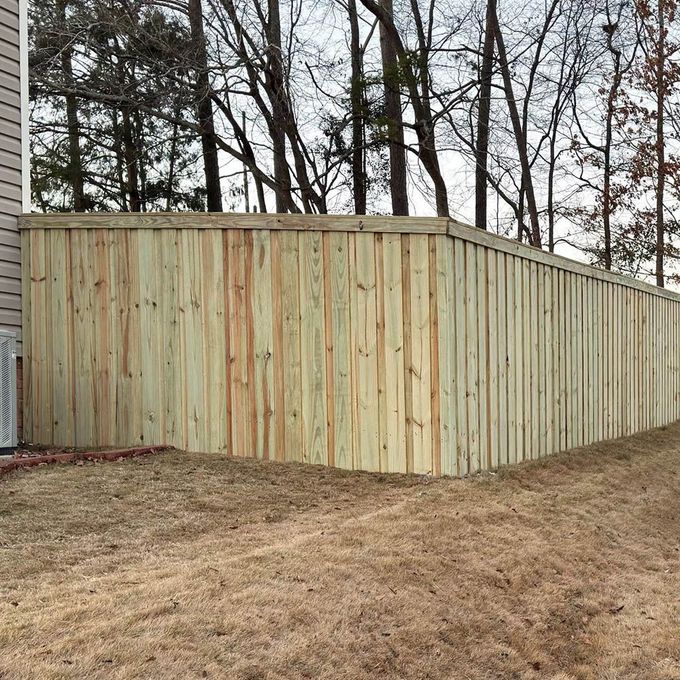 A wooden fence is surrounded by trees in a backyard.