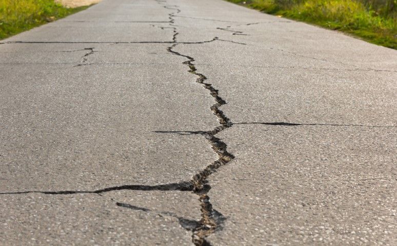 Cracked asphalt road, likely caused by earthquake damage, stretches into the distance.