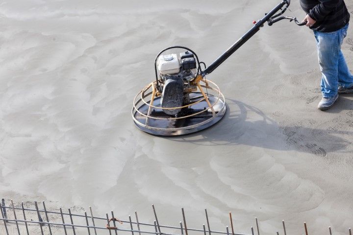 Person operating a power trowel on a newly poured concrete surface.