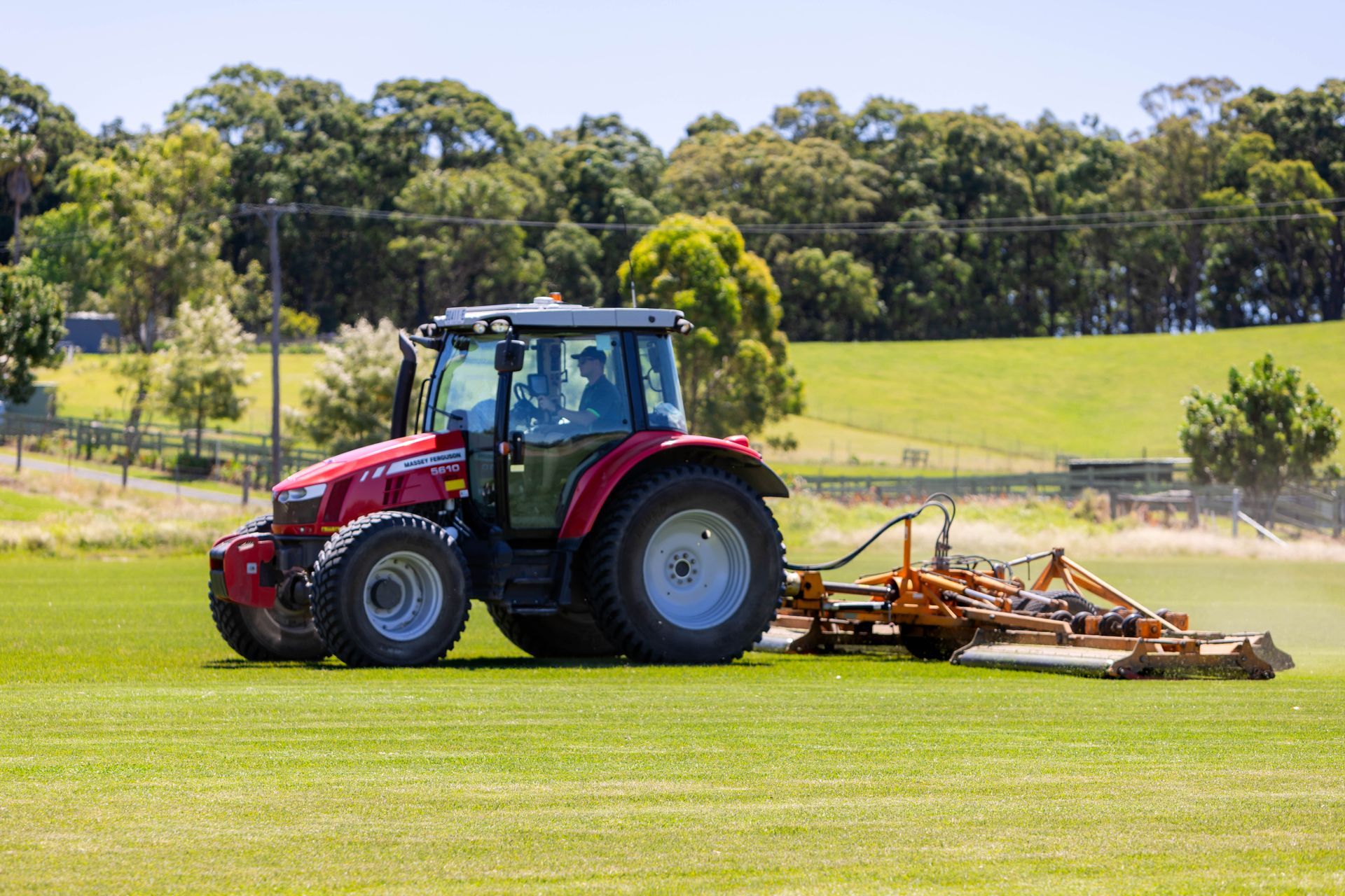 Red tractor mowing grass on a green field, rear view with attached mower deck.