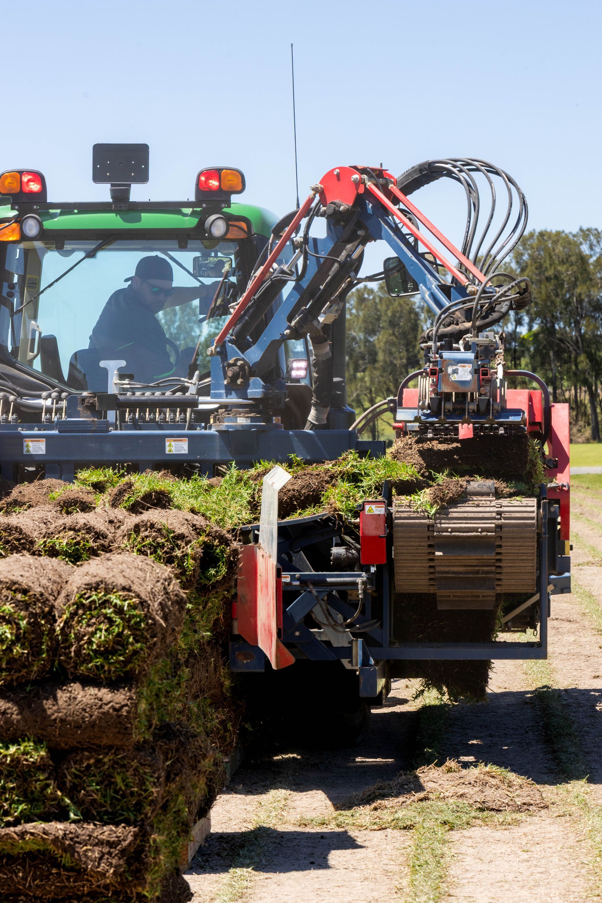 A tractor with a mechanical arm harvests and stacks rolled sod in a field.