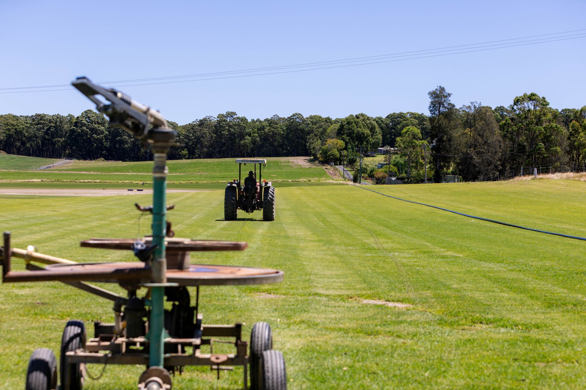 Tractor pulling irrigation equipment across a green field; trees and blue sky in background.