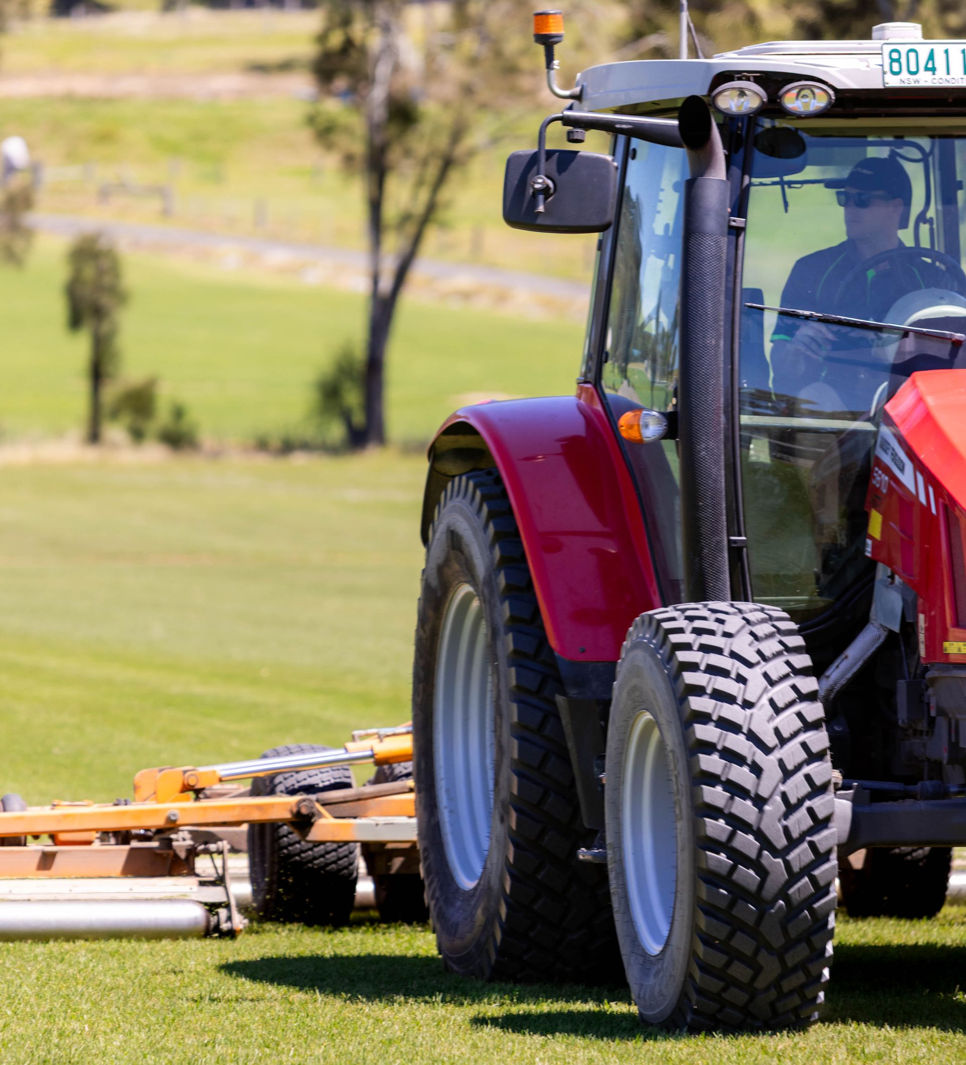 Tractor on field harvesting sod rolls, blue sky.
