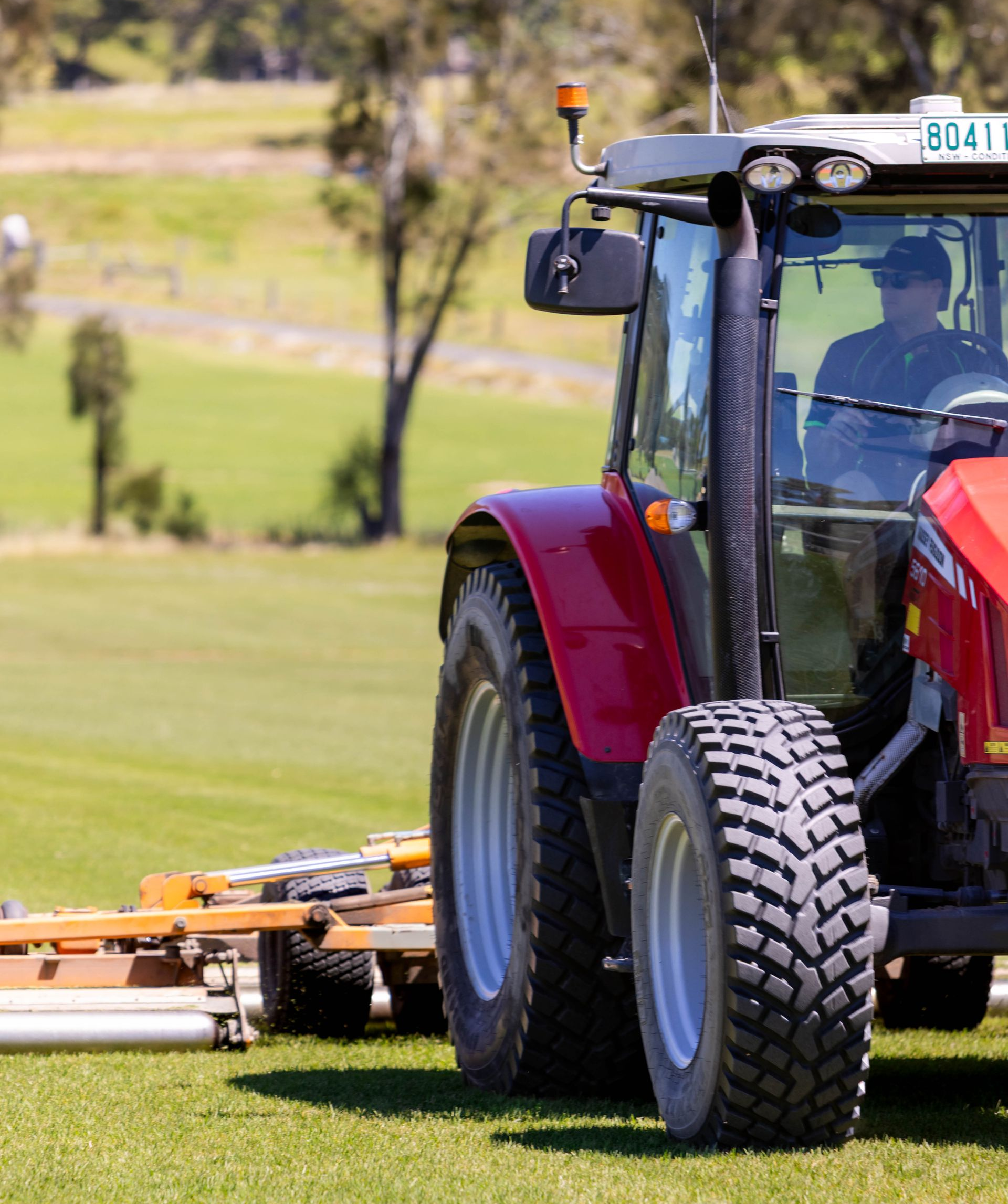 Red tractor mowing green grass in a field.