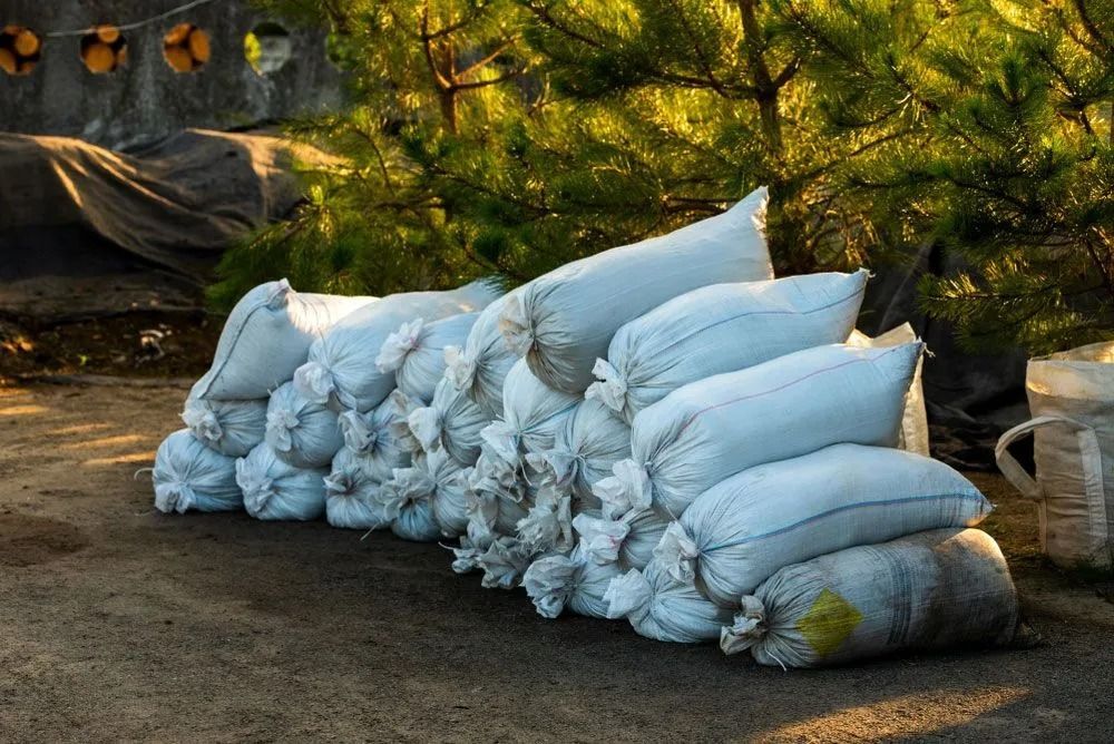 Pile of white sacks on a paved surface outdoors, likely containing some material, with trees in the background.
