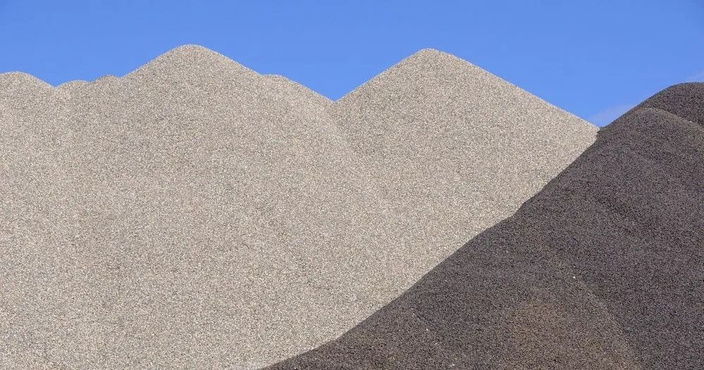 Piles of light gray and dark gray gravel or sand against a clear blue sky.