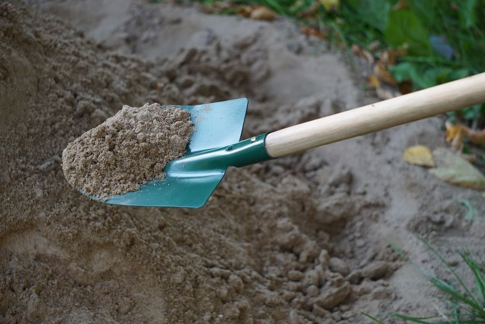 Shovel holding a scoop of sand. Green shovel in a pile of sand outdoors with a light-colored handle.