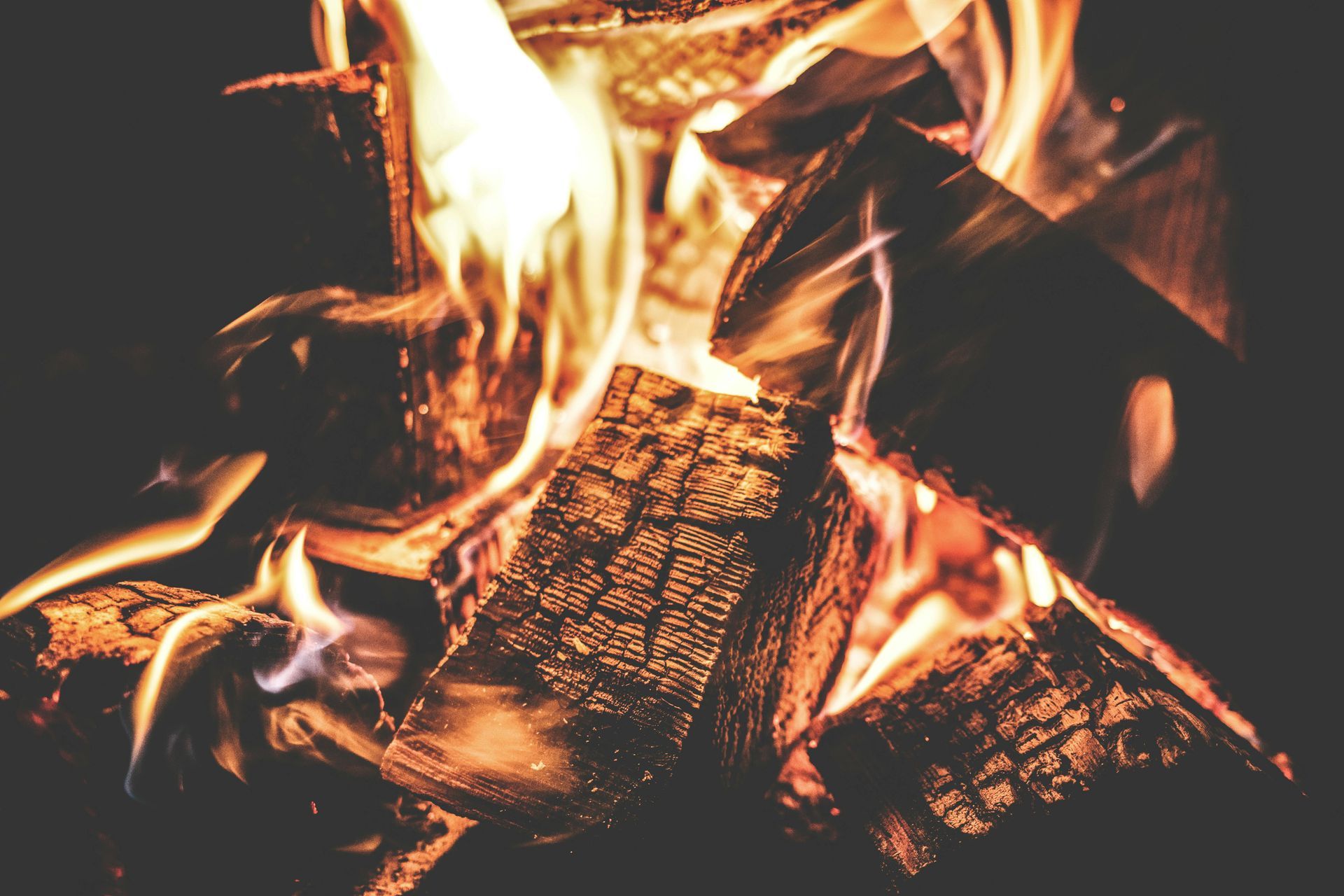 Burning firewood, flames are orange and yellow against a dark background.